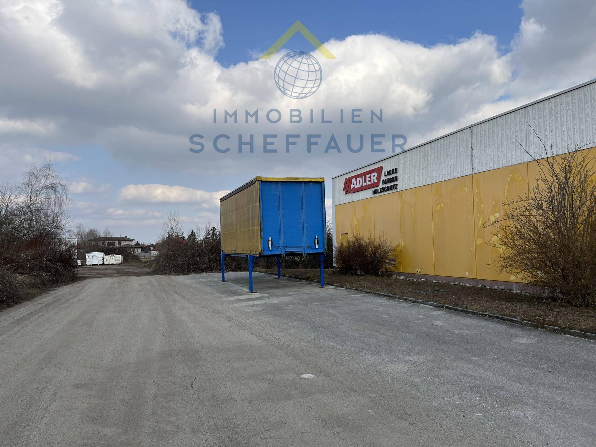 Außenansicht eines Gewerbegebäudes mit einem blauen Anhänger und weitem Gelände unter bewölktem Himmel.