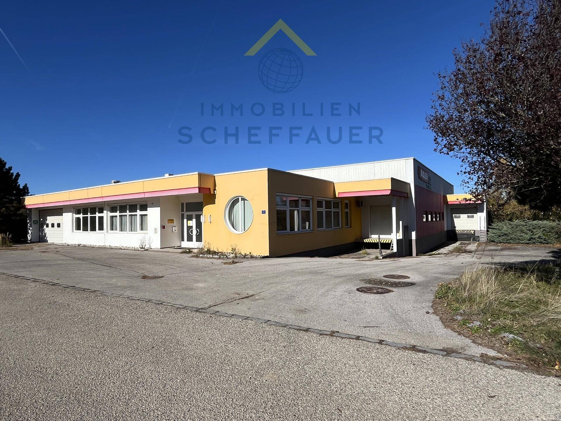 Gebäudeansicht eines Gewerbeobjekts mit gelber Fassade und großem Parkplatz unter blauem Himmel.