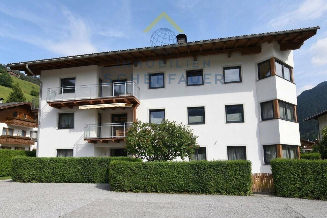 Weiße Fassade eines Wohnhauses mit Balkonen und gepflegter Hecke im Vordergrund.