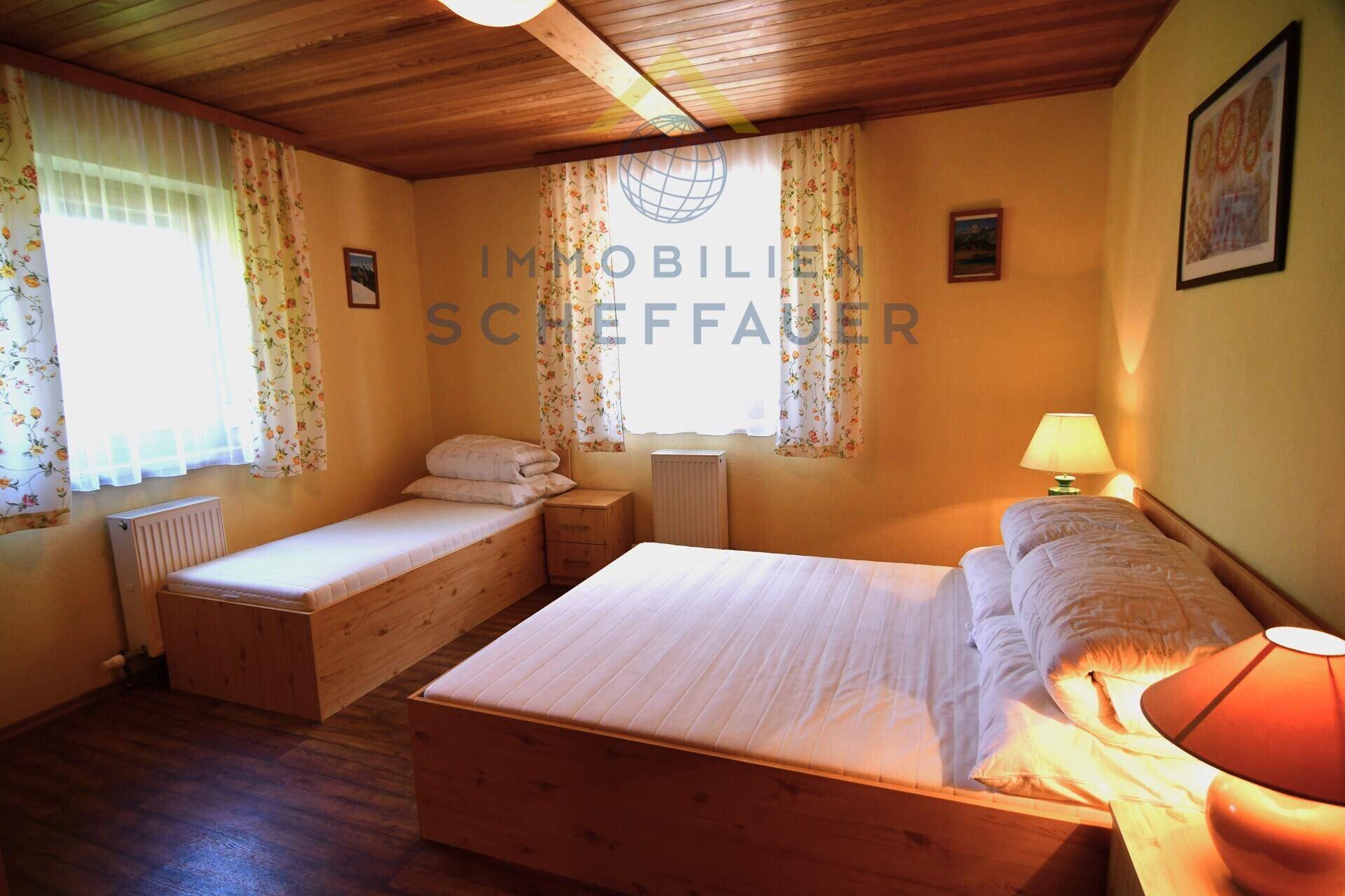 Helles Schlafzimmer mit zwei Betten, Holzvertäfelung an der Decke und rustikalen Möbeln.