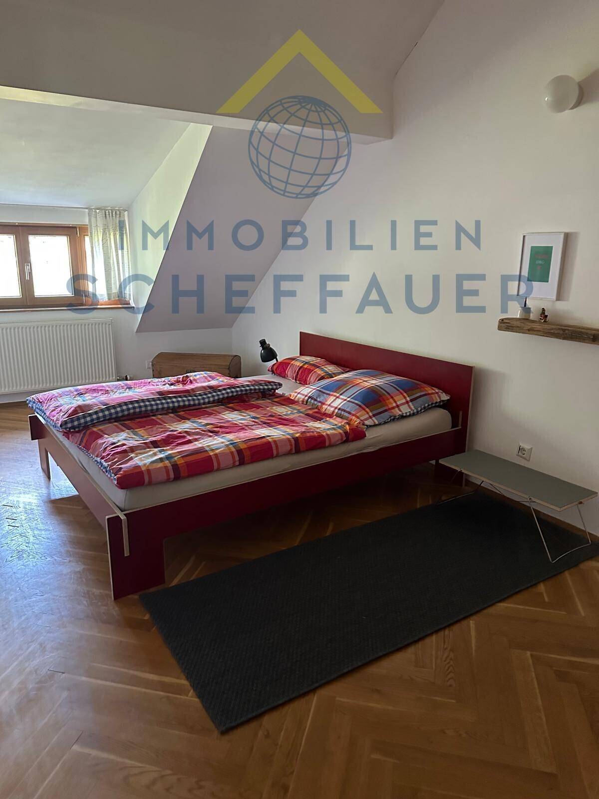Helles Schlafzimmer mit Parkettboden, rotem Bettrahmen und schrägen Wänden unter dem Dach.
