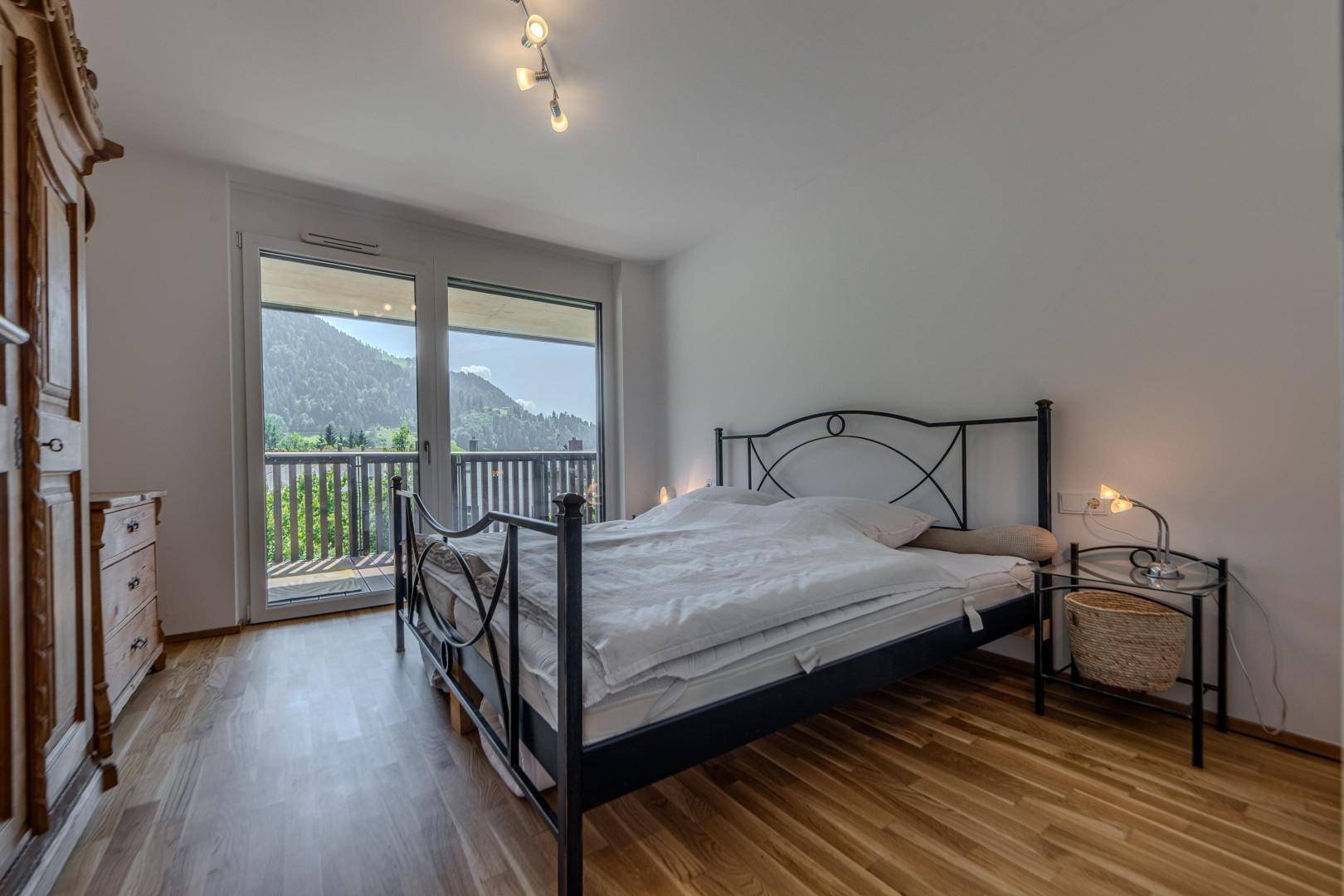 Schlafzimmer mit Doppelbett, Holzboden und Balkonzugang mit Bergblick.