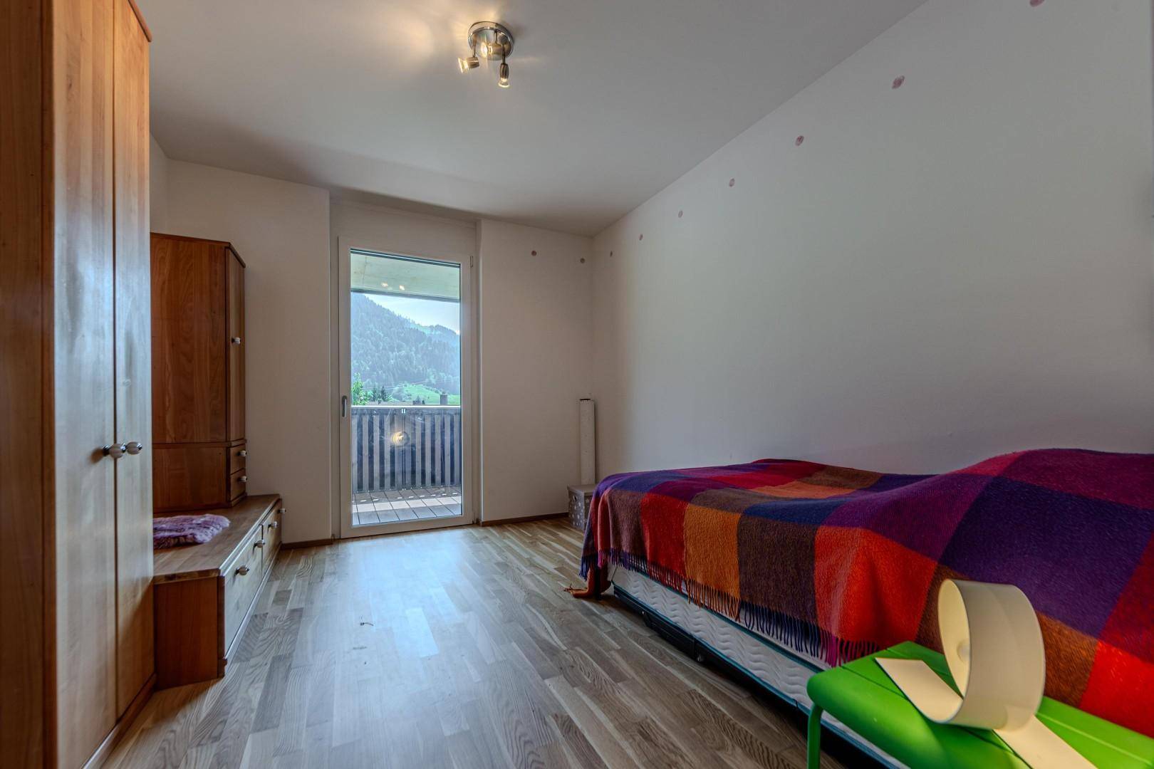 Schlafzimmer mit Einzelbett, Holzboden und Balkonzugang mit Bergblick.