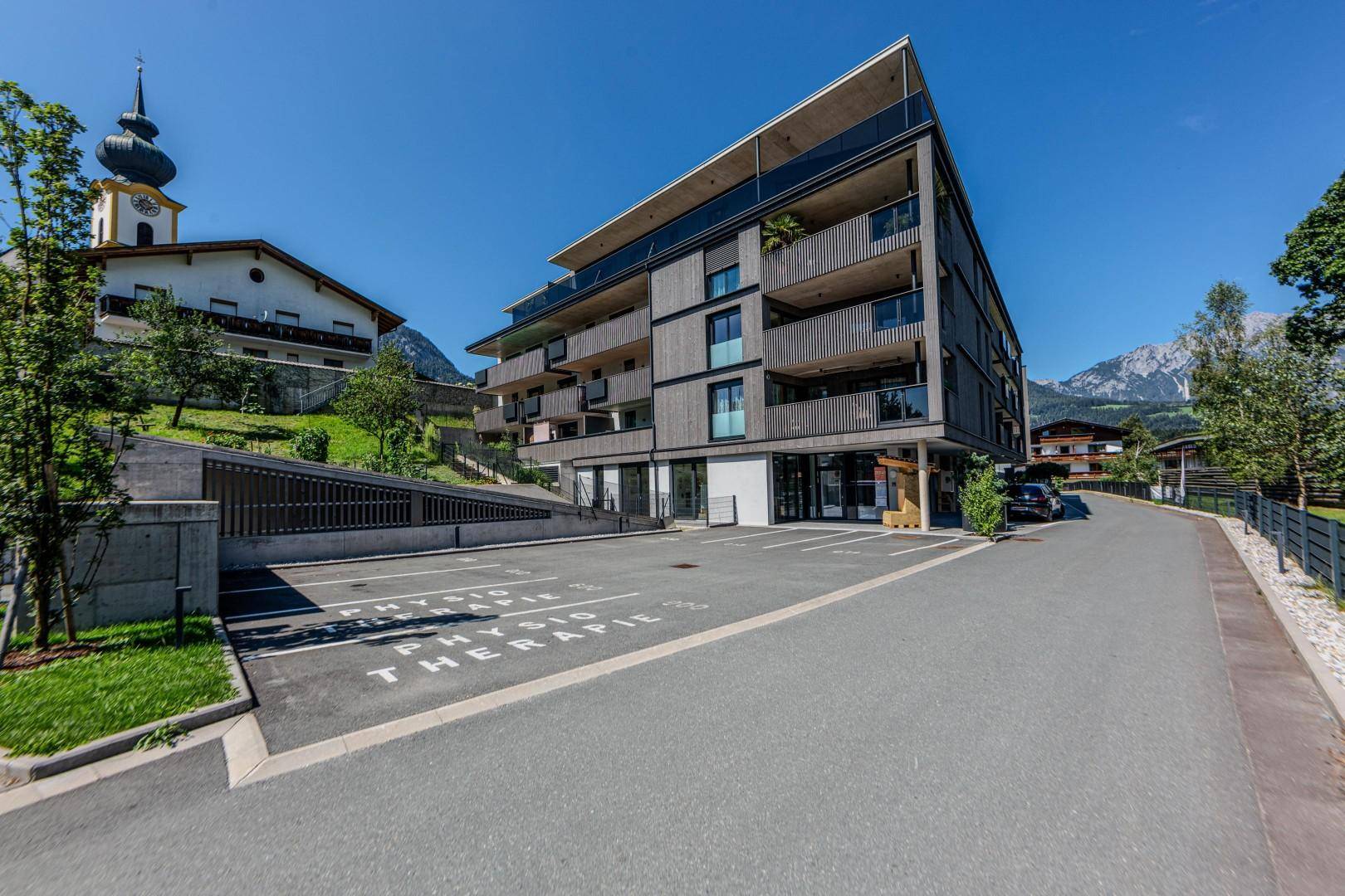 Modernes Wohngebäude mit Tiefgaragenzufahrt und umliegender grüner Landschaft.