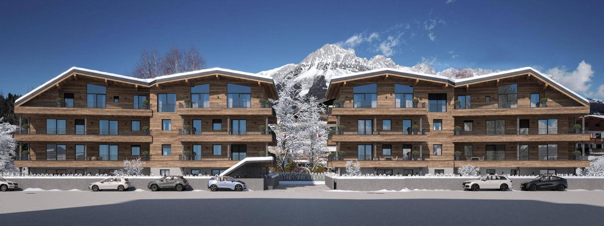 Moderne Apartmentanlage mit Holzfassade, großen Fenstern und Balkonen vor einer beeindruckenden Bergkulisse im Winter.