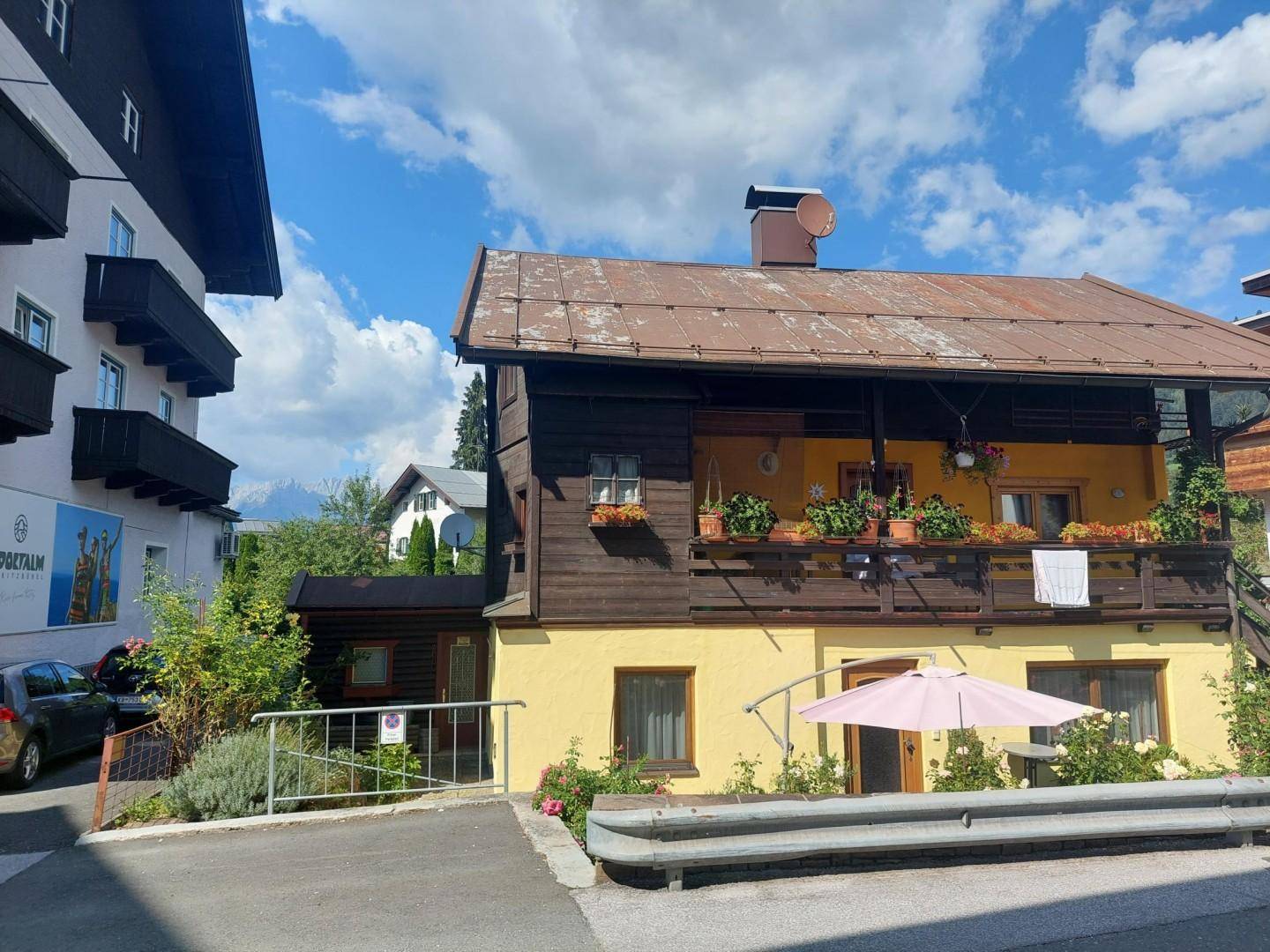 Traditionelles Gebäude mit Holzbalkonen, Blumenkästen und gelber Fassade in alpiner Umgebung.