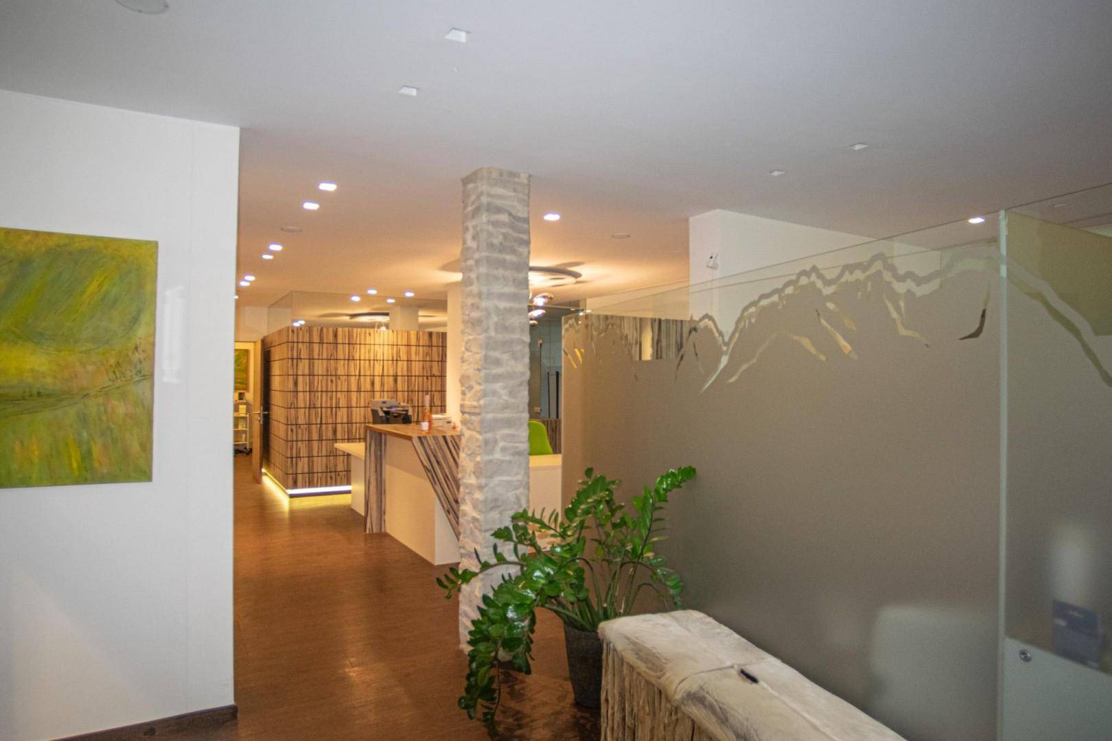 Heller Flur mit Holzboden, einer Steinsäule und dekorativen Glaswänden mit Bergmotiv.