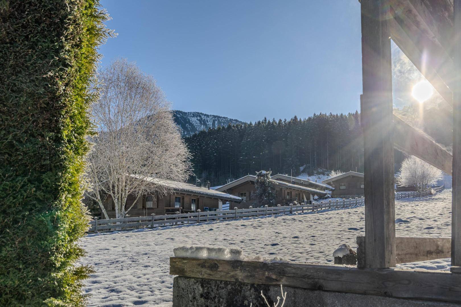 Malerische Winterlandschaft mit verschneiten Hütten und Bäumen unter strahlend blauem Himmel.