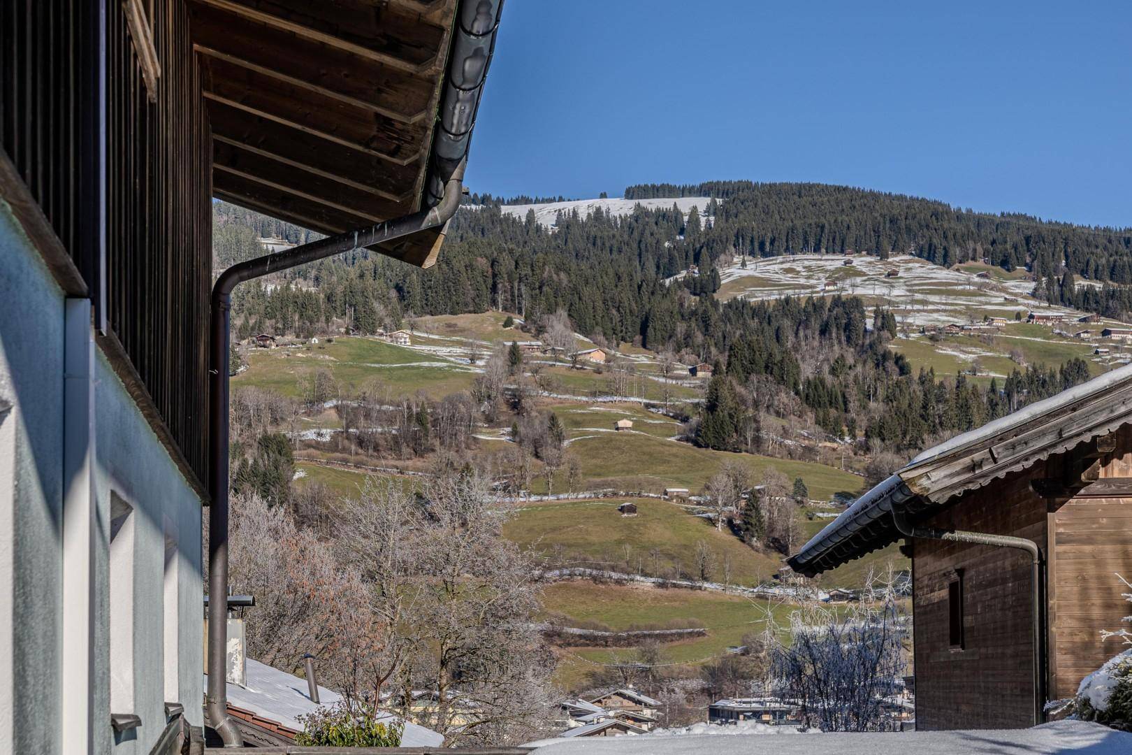 Weitläufiger Blick auf die verschneite Berglandschaft mit grünen Hängen und Wäldern.