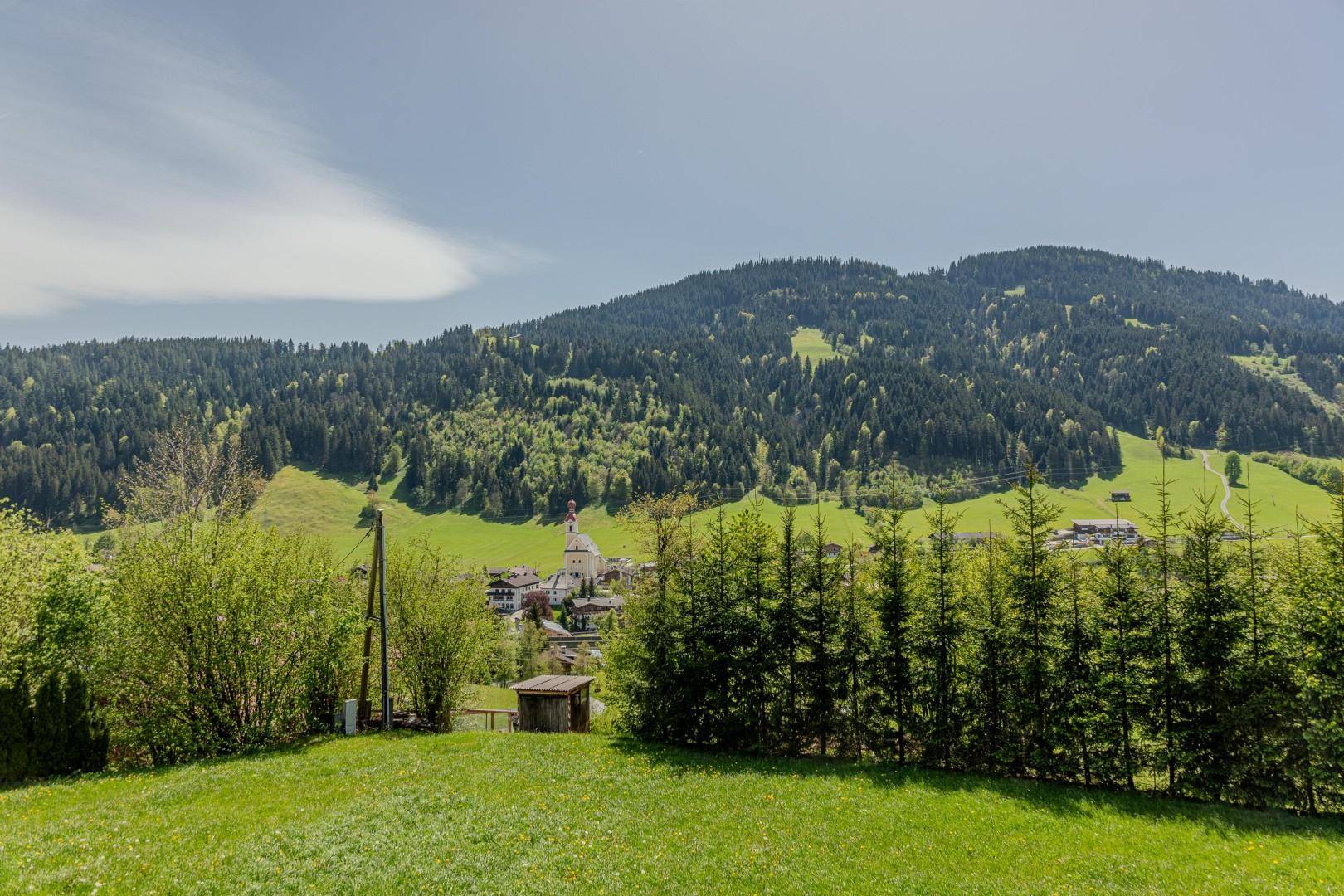 Weitläufiger Blick auf ein charmantes Dorf mit Kirche, eingebettet in eine grüne Berglandschaft.