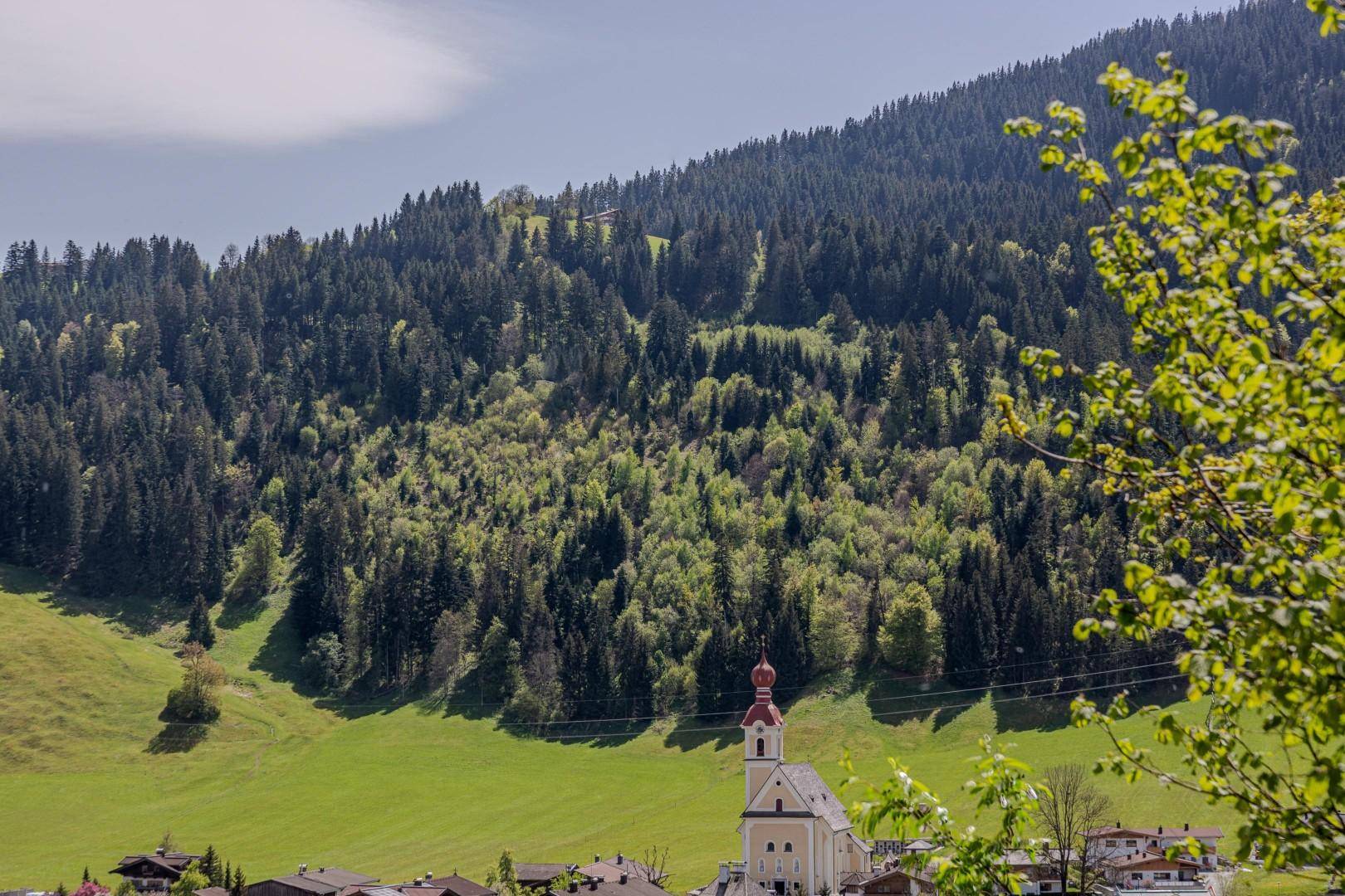 Malerisches Dorf mit einer Kirche, eingebettet in eine grüne Hügellandschaft mit dichten Wäldern.