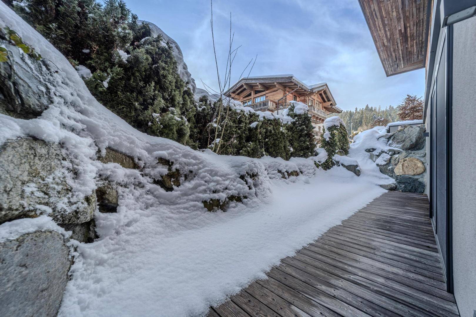 Holzdeck im Schnee, umgeben von Felsen und Bäumen, führt zum Gebäude.