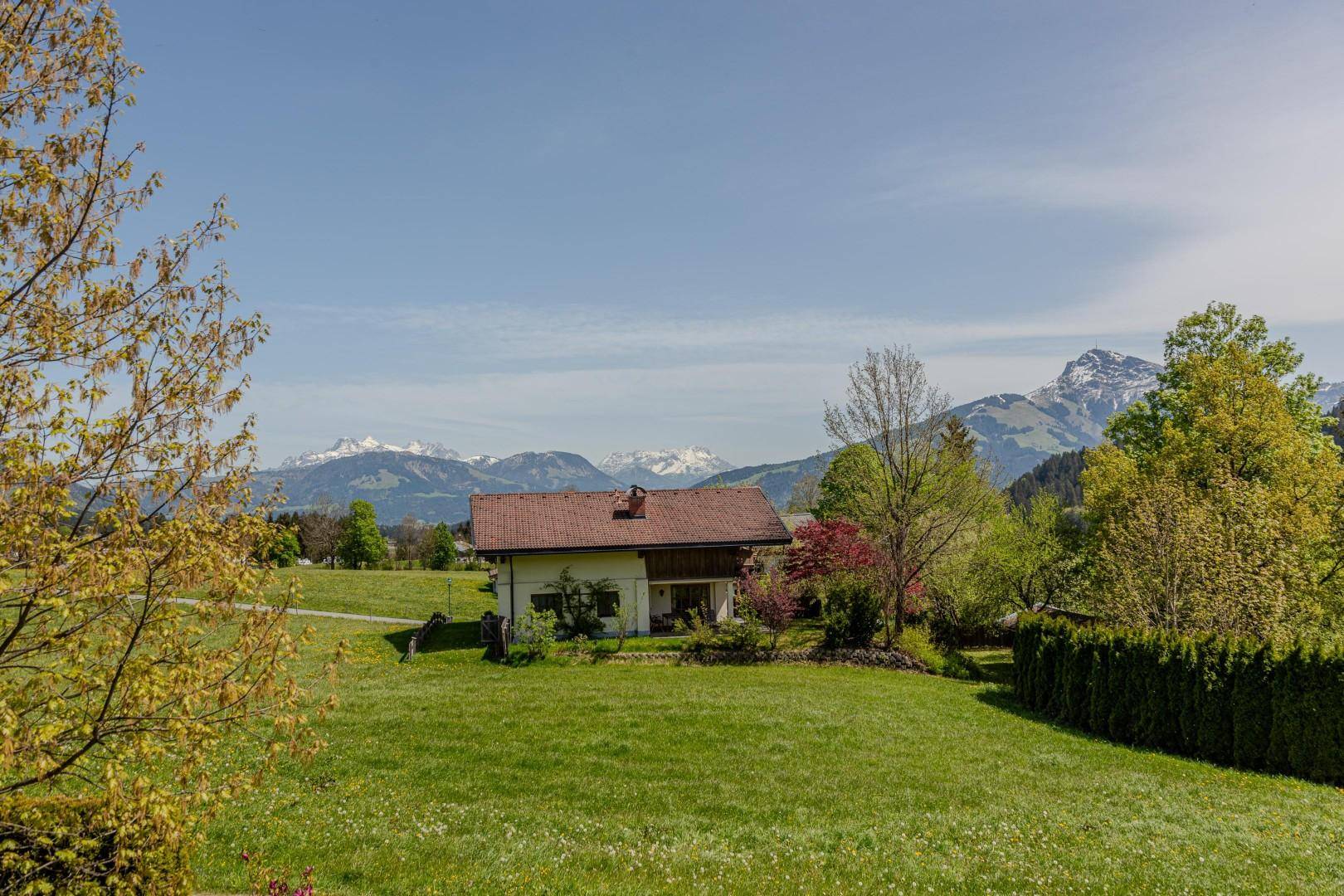 Idyllisches Einfamilienhaus mit rotem Dach in einer grünen Hügellandschaft mit fernen Bergen.
