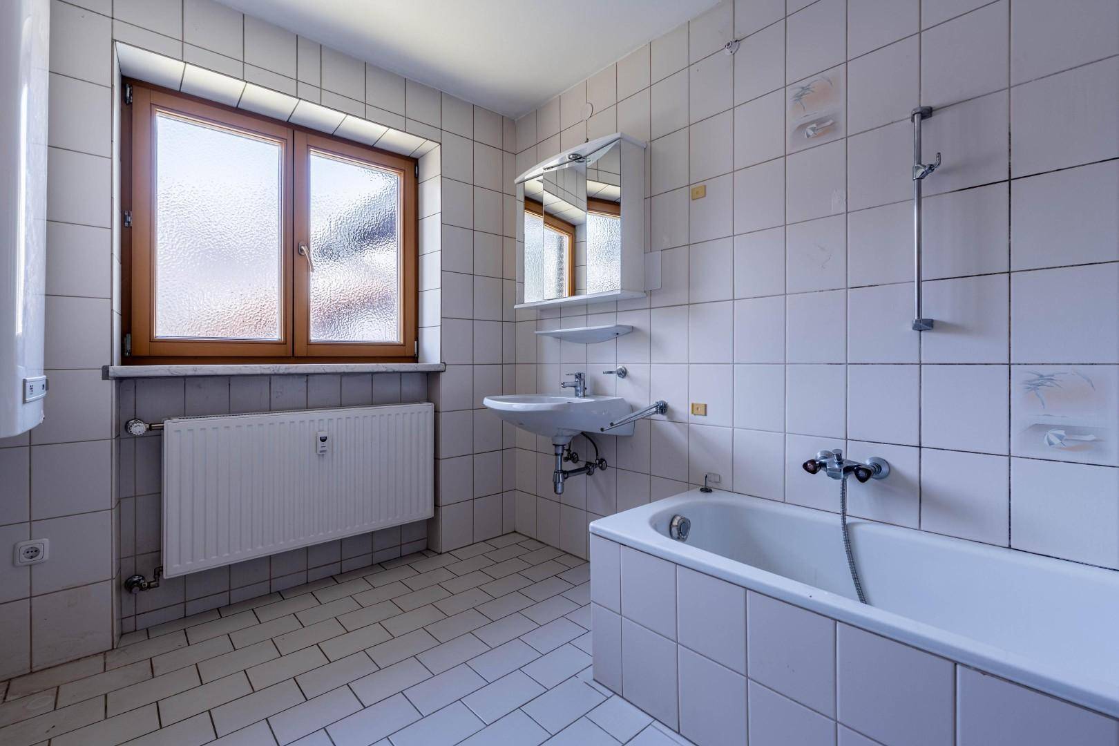 Badezimmer mit weißen Fliesen, Badewanne, Waschbecken und Spiegelschrank, gut beleuchtet.