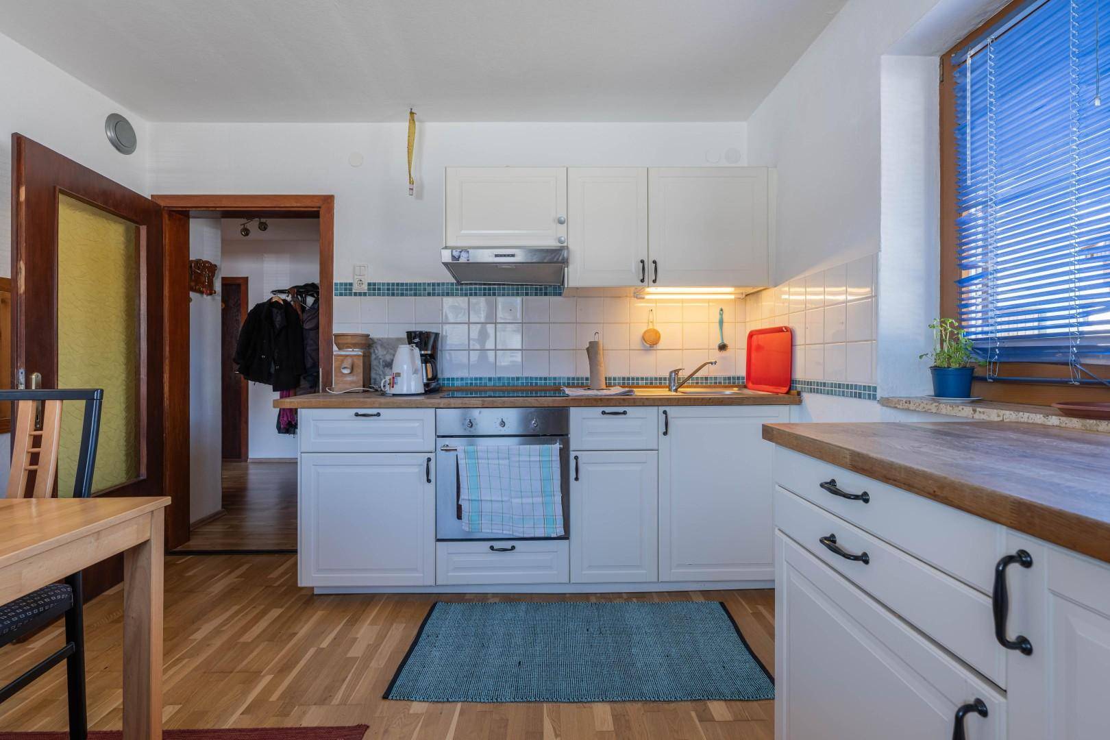 Funktionale Küche mit weißen Schränken, Holz-Arbeitsplatte und Fliesen-Rückwand, gut beleuchtet.