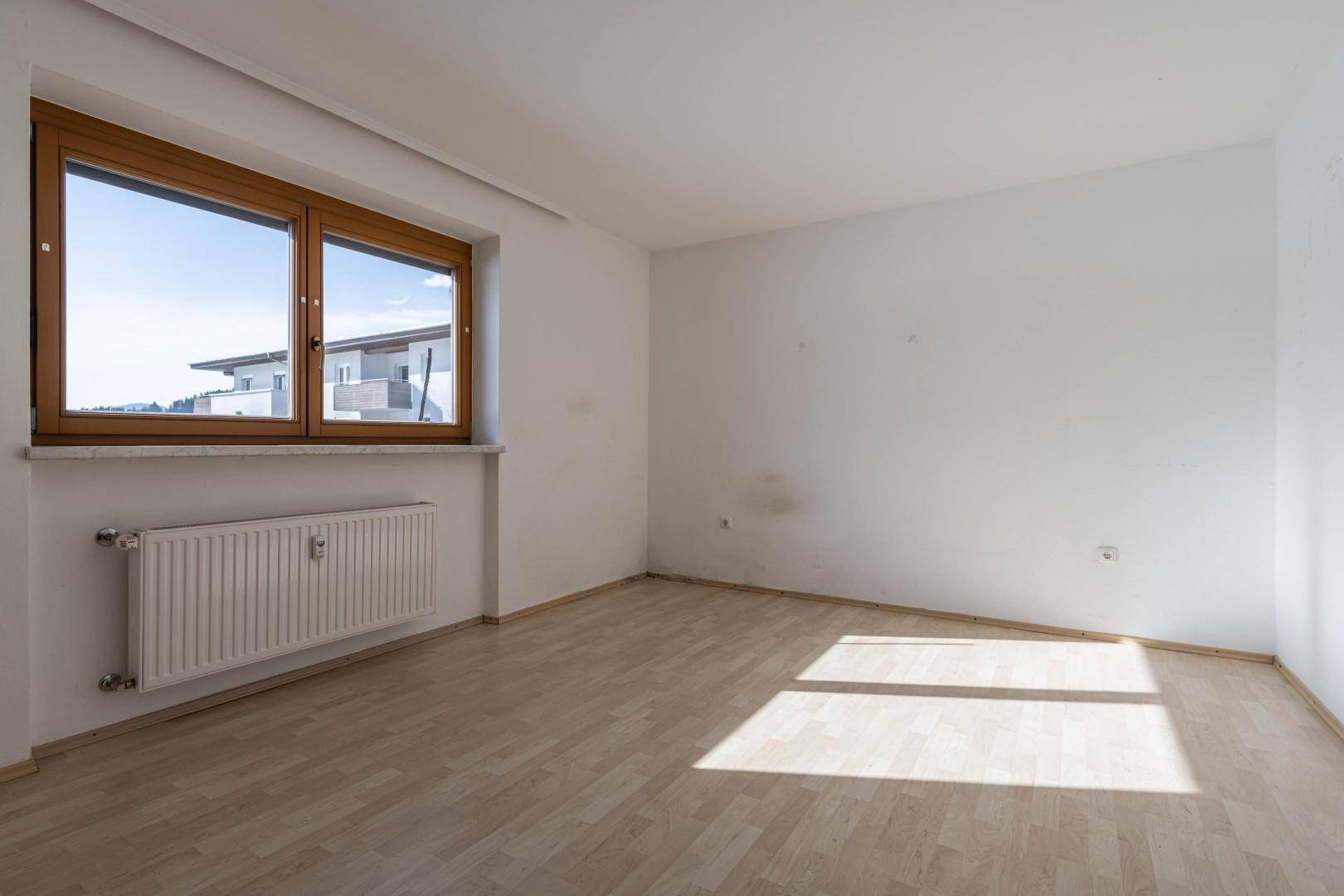 Helles, leeres Zimmer mit Holzdielenboden und großem Fenster, ideal für individuelle Gestaltung.