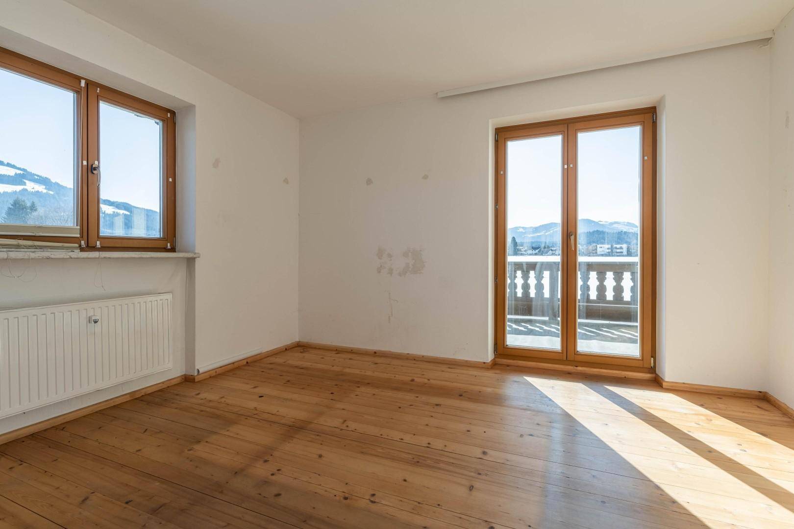 Leeres Zimmer mit Holzdielenboden und Zugang zu einem Balkon, bietet viel natürliches Licht.