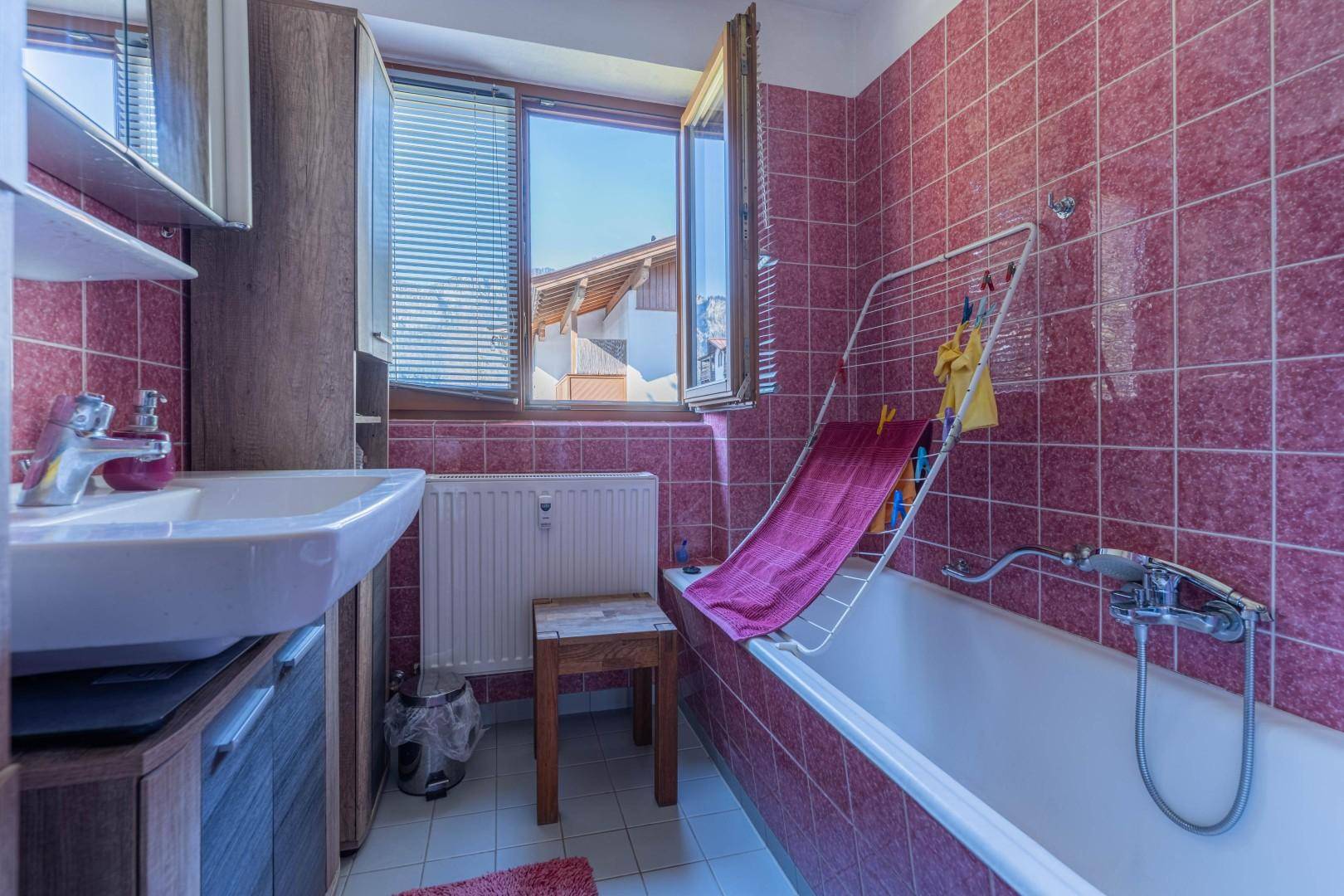 Badezimmer mit rosa Fliesen, Badewanne, Waschbecken und Fenster für natürliche Belüftung.