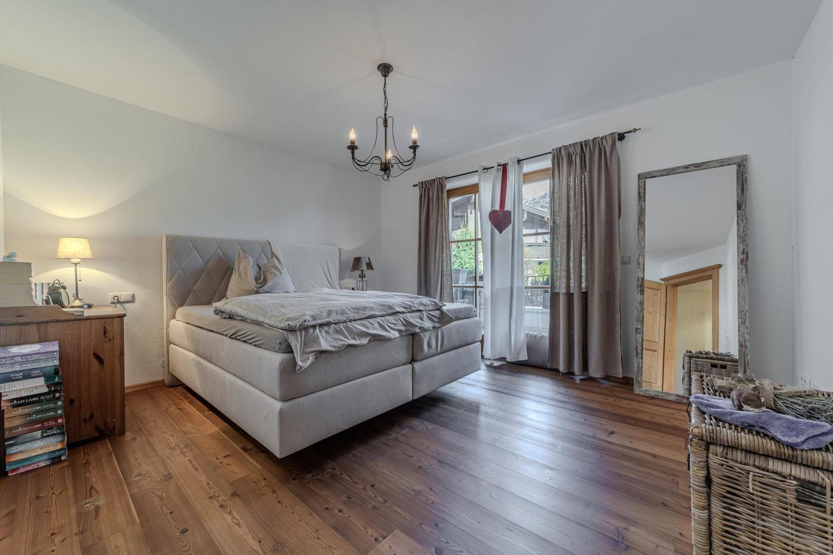 Geräumiges Schlafzimmer mit Holzboden, Doppelbett und Zugang zum Balkon.