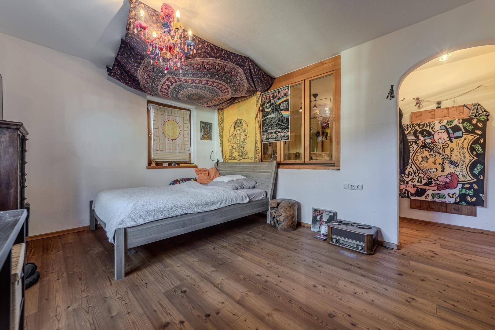 Gemütliches Schlafzimmer mit Holzboden und kreativer Wandgestaltung, viel Tageslicht.