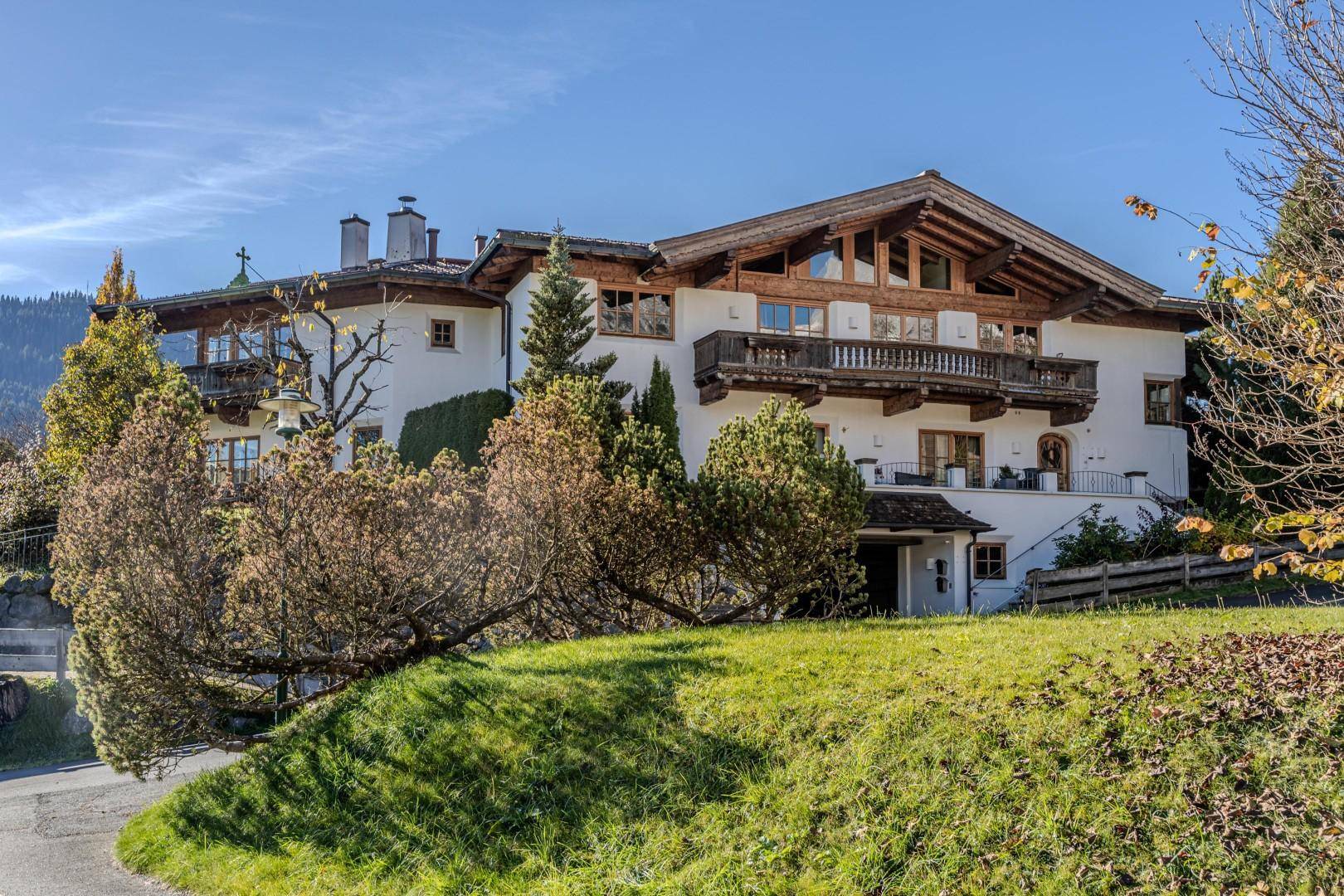 Traditionelles alpenländisches Haus mit Holzbalkonen und weißer Fassade, umgeben von Grünflächen.