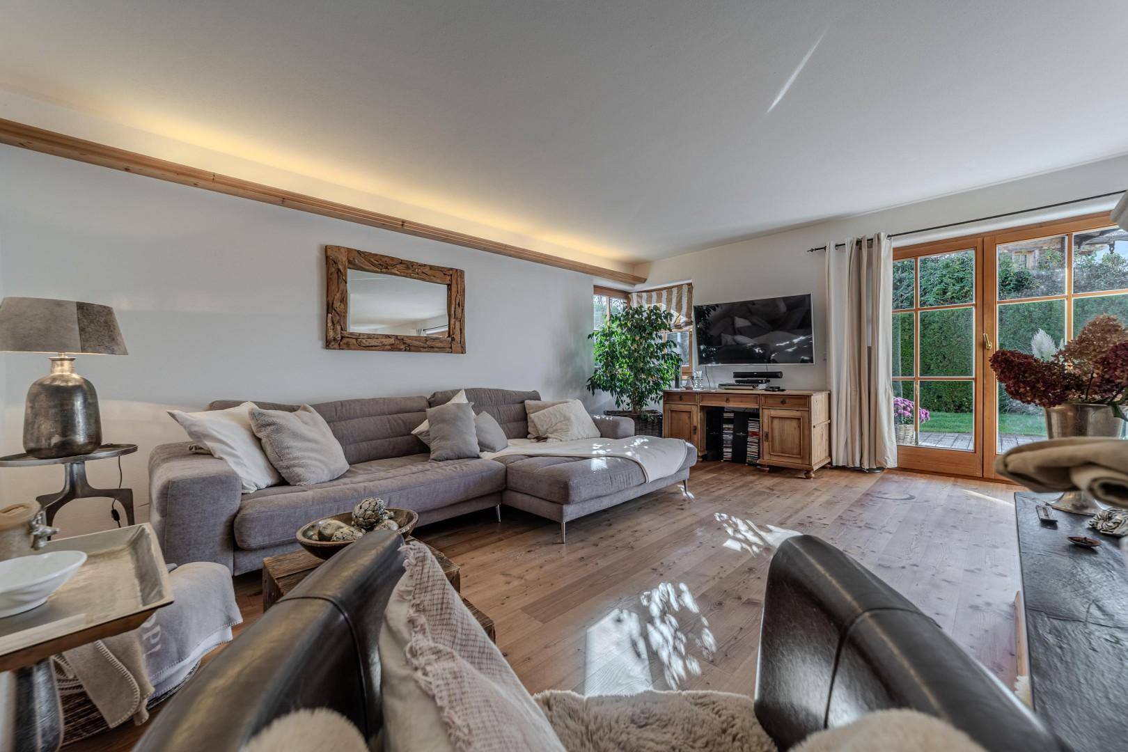 Lichtdurchflutetes Wohnzimmer mit Holzboden, großem Sofa und Zugang zum Garten.