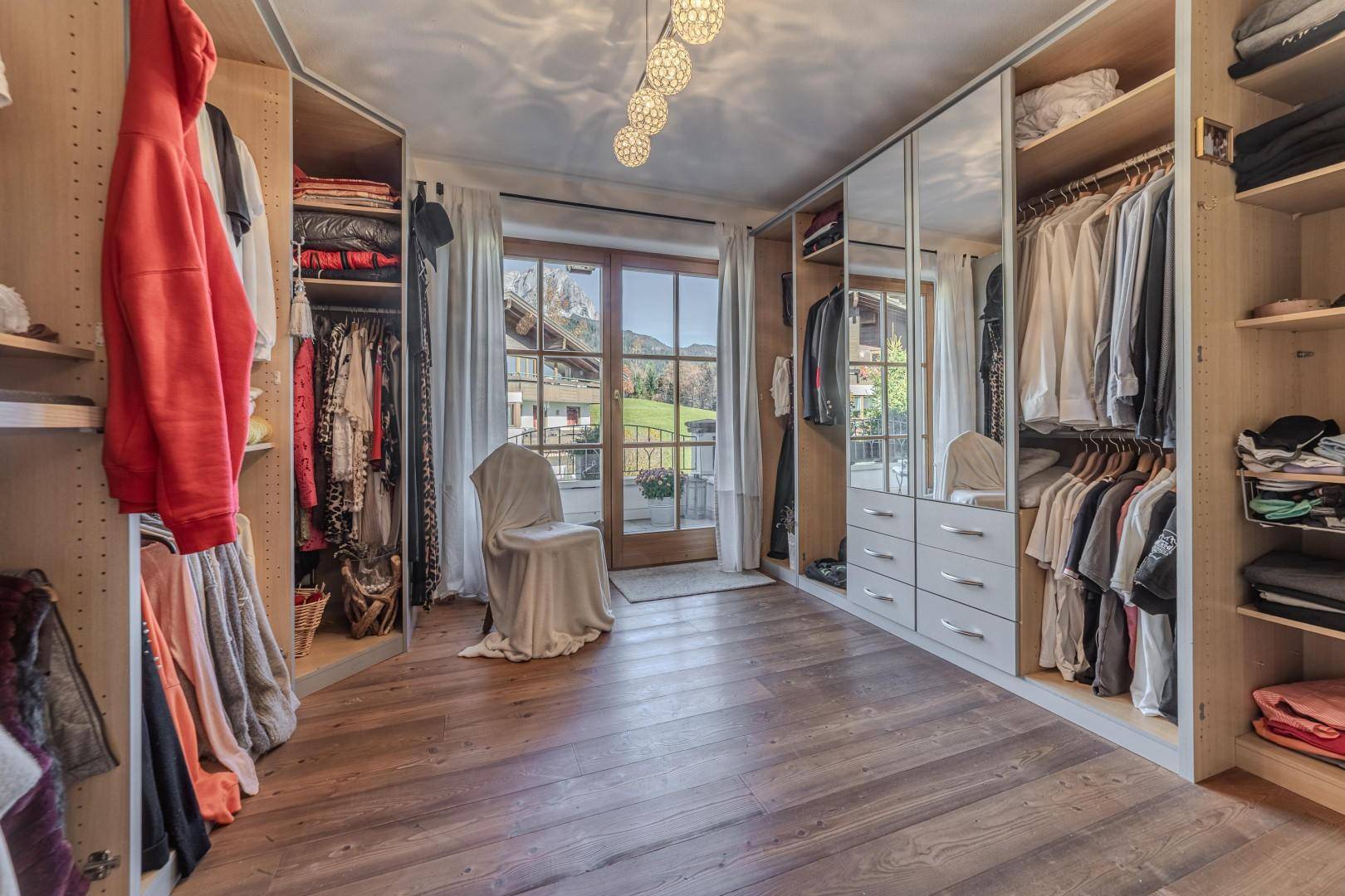 Begehbarer Kleiderschrank mit viel Stauraum, Holzboden und Balkonzugang.