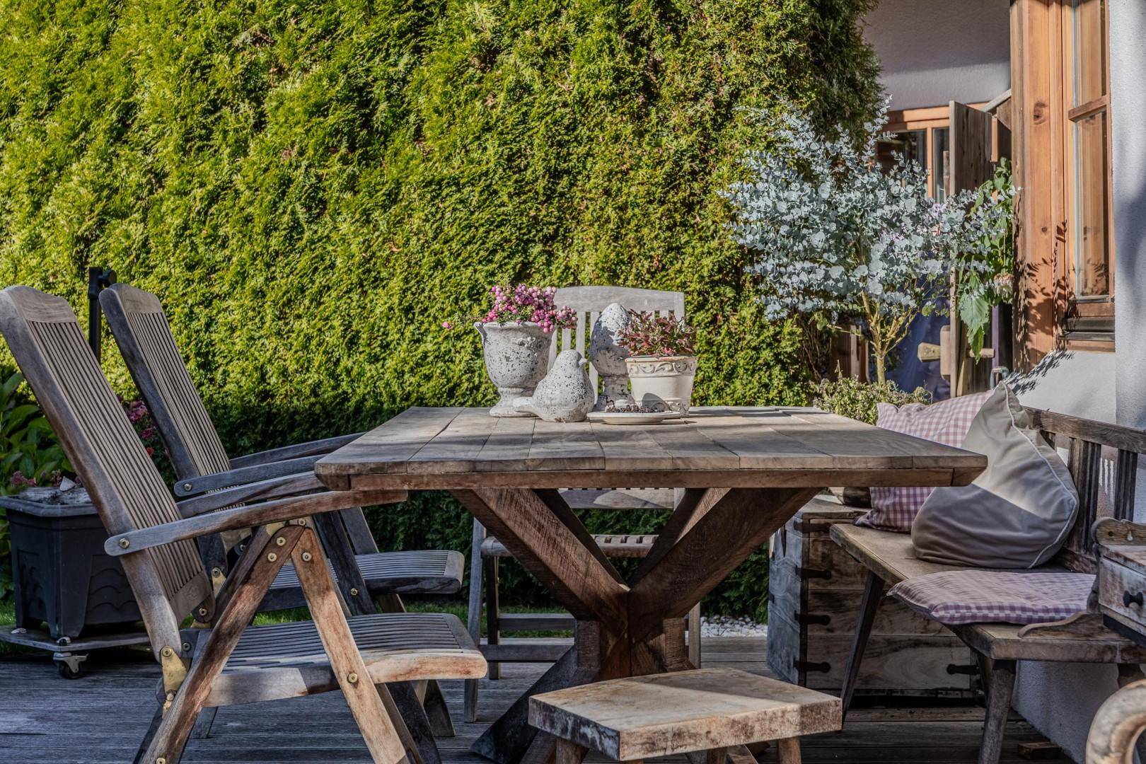 Gemütliche Holzterrasse mit rustikalen Gartenmöbeln, umgeben von grüner Hecke.