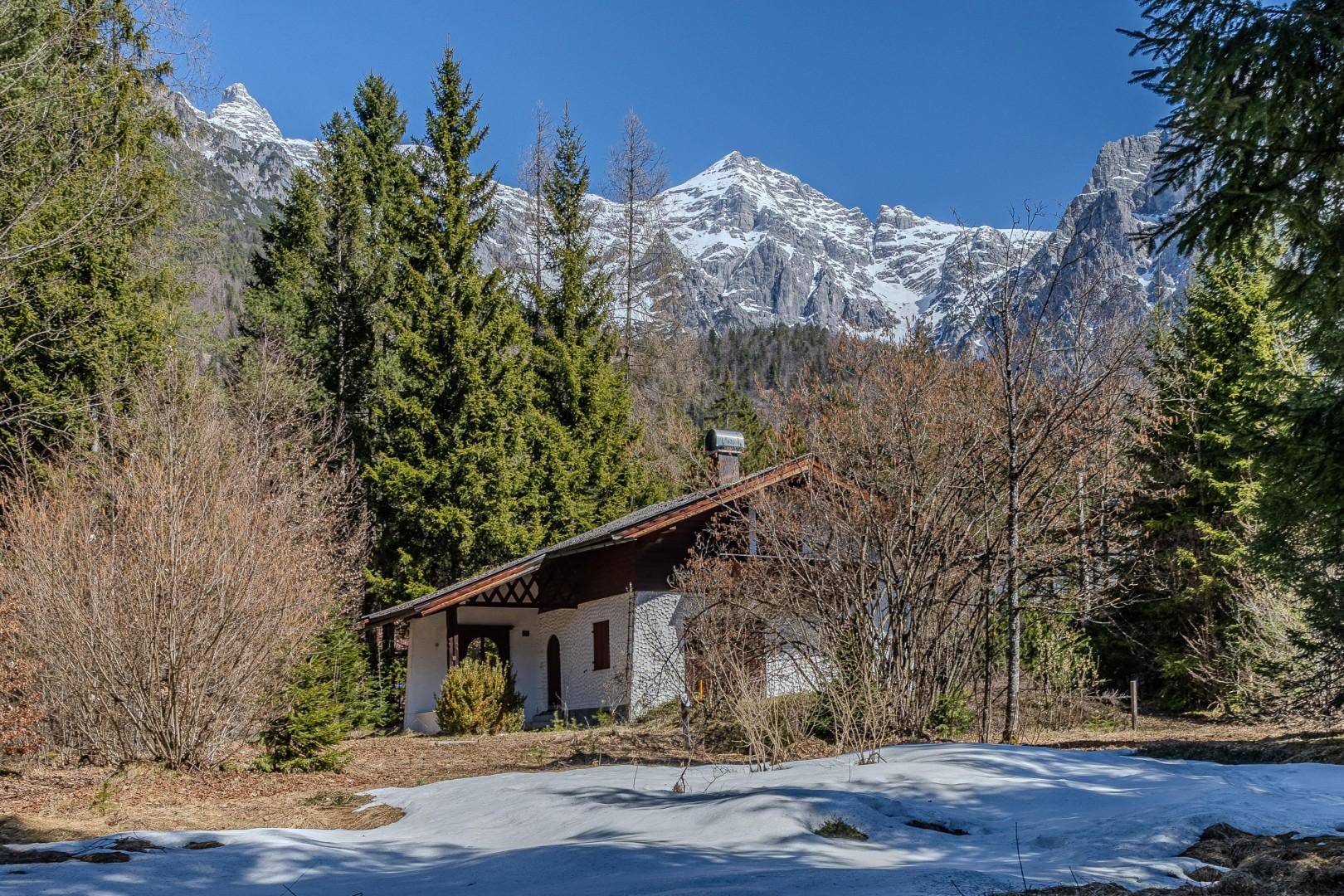Idyllisches Haus in den Bergen mit schneebedeckten Gipfeln und umgebender Natur.