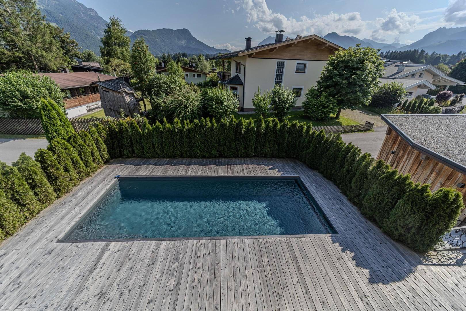 Außenbereich mit rechteckigem Pool und Holzdeck, umgeben von Hecken und Blick auf die umliegende Natur.