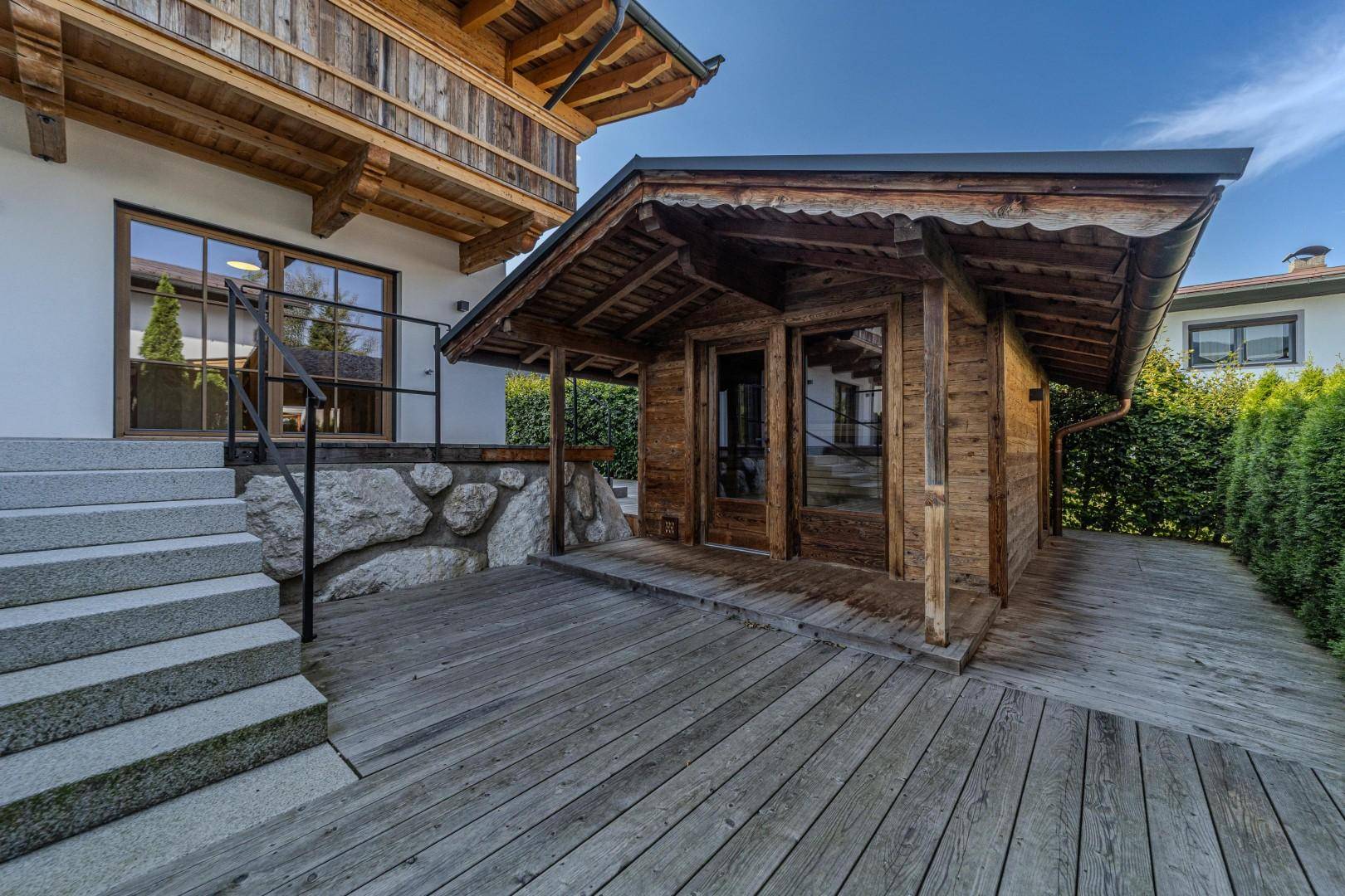 Außenbereich mit Holzterrasse und separatem Holzhaus, umgeben von Natur und mit Zugang zum Hauptgebäude.