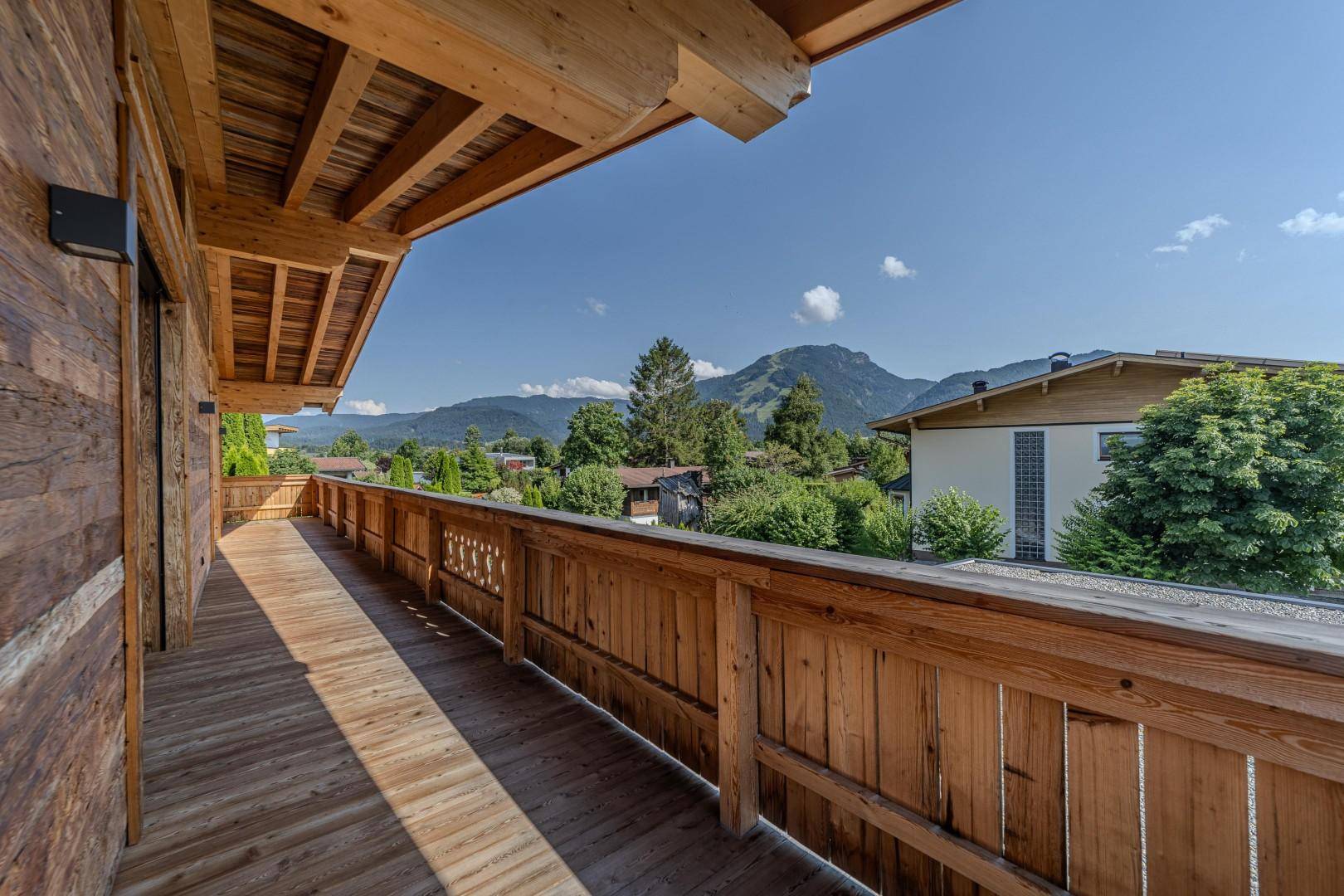 Langer Holzbalkon mit Bergblick und viel Sonnenschein, ideal zum Entspannen im Freien.