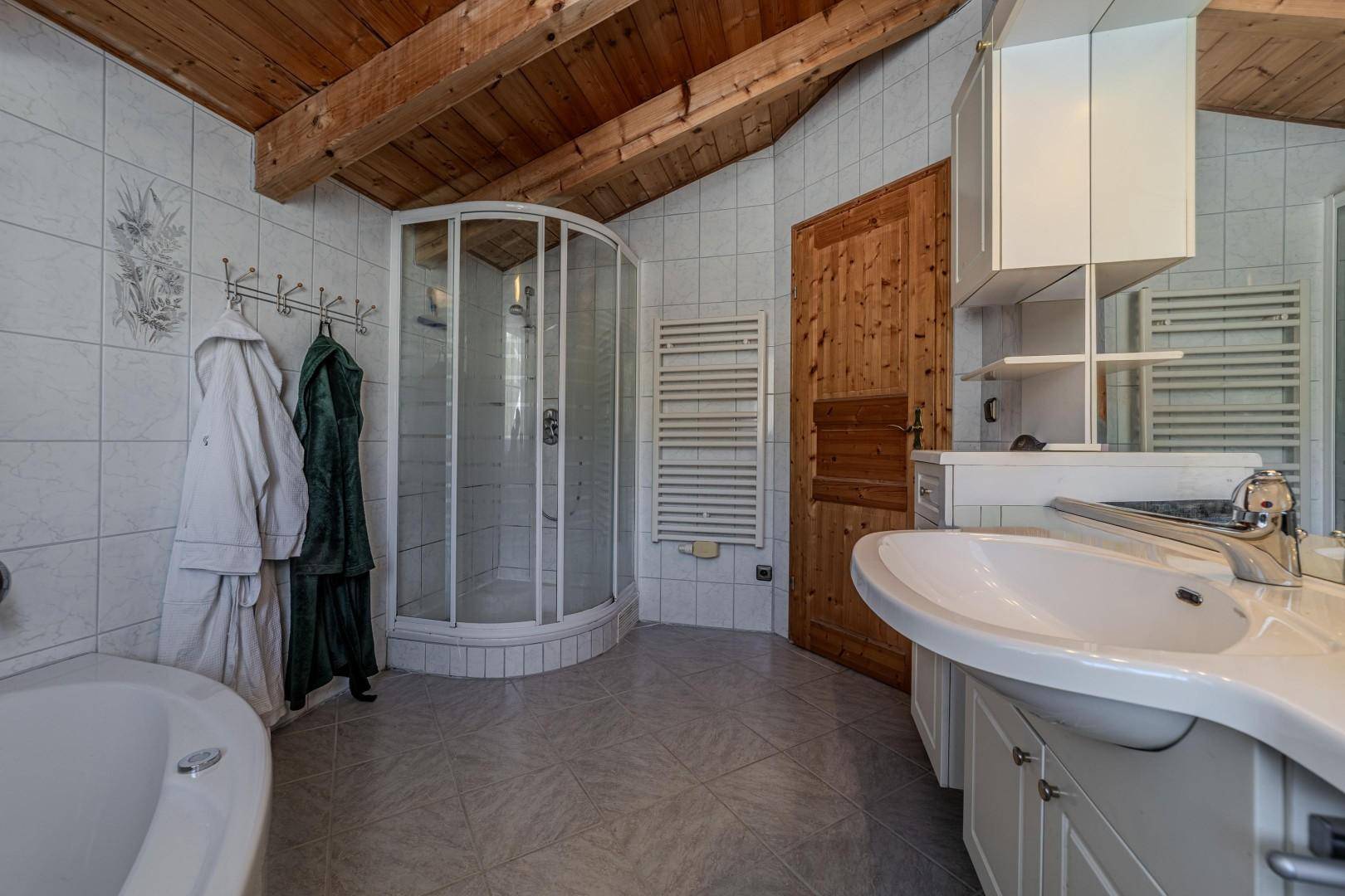 Badezimmer mit Dusche, Waschtisch und beheiztem Handtuchhalter unter Holzbalkendecke.