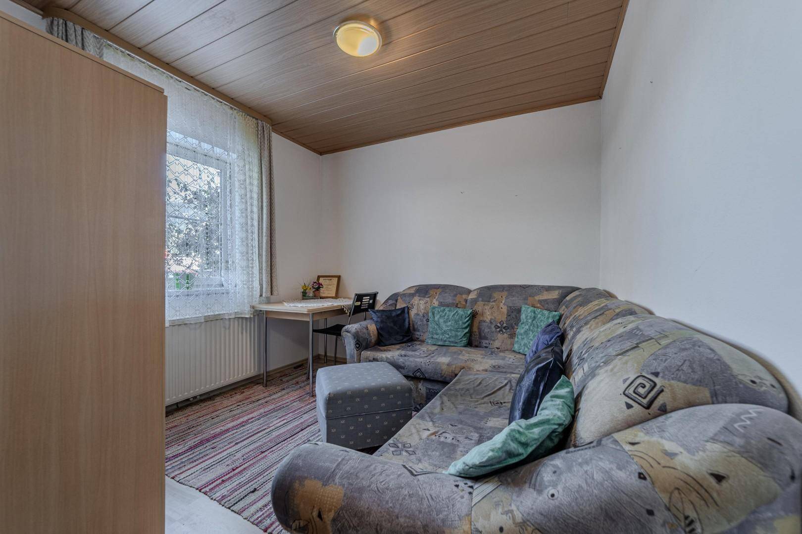 Kleiner Wohnbereich mit Ecksofa, Teppichboden und Holzdeckenverkleidung.