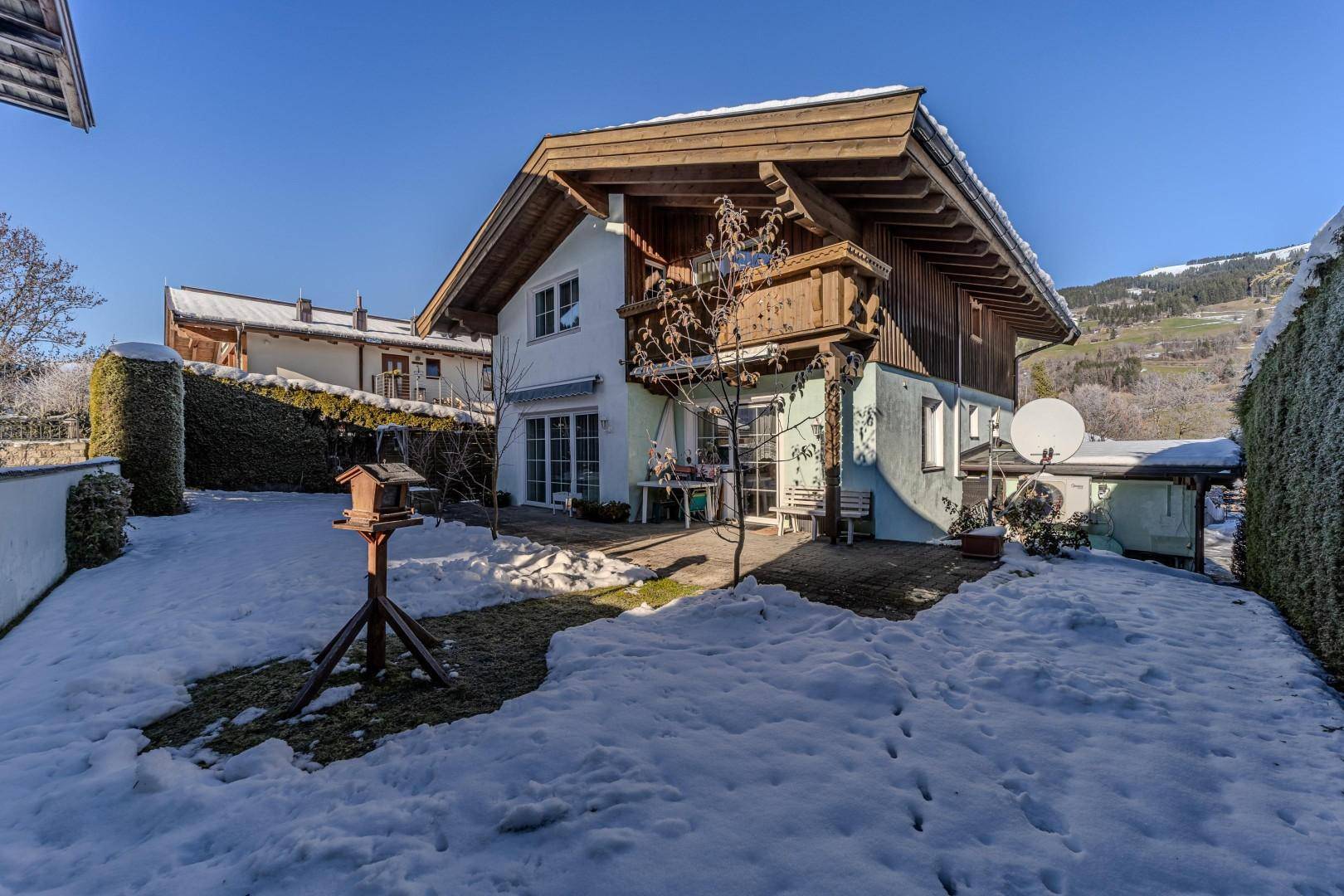 Winterlicher Garten mit Terrasse, Vogelhaus und Blick auf die Berge.