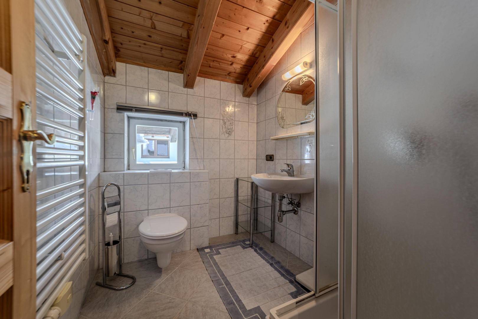 Kleines Badezimmer mit Dusche, WC, Waschbecken und Fenster.