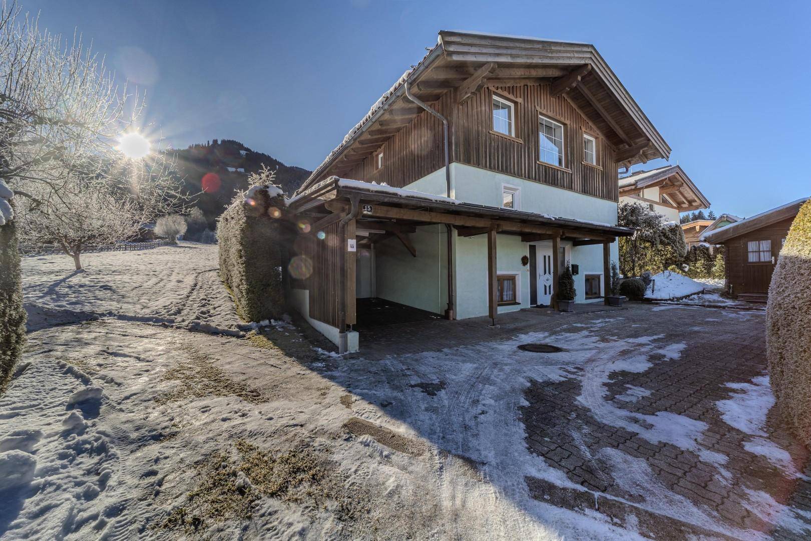 Hausansicht im Winter mit Carport, Auffahrt und sonniger Umgebung.
