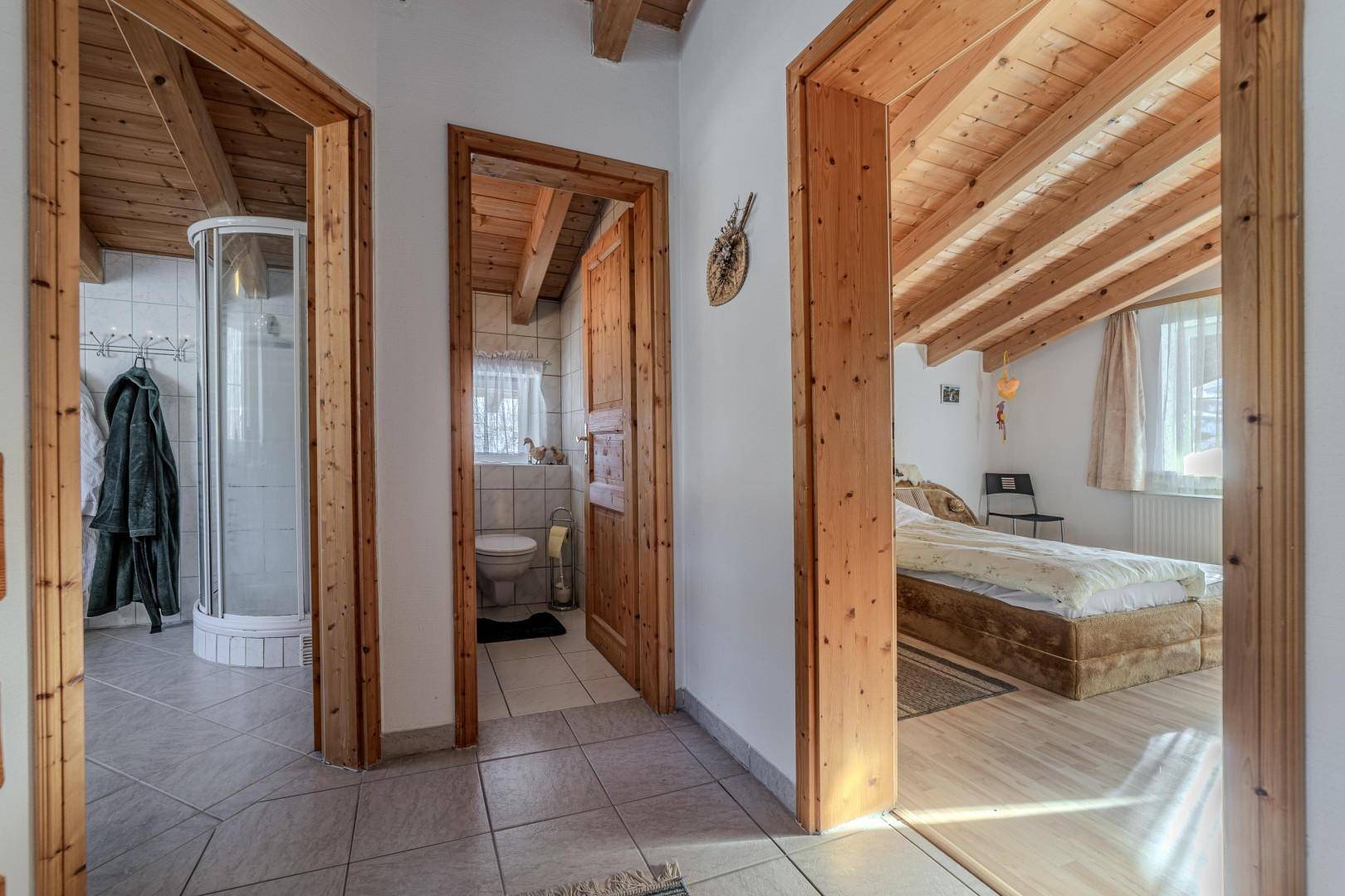 Flur im Dachgeschoss mit Zugang zu Schlafzimmer, Bad und WC unter Holzbalkendecke.