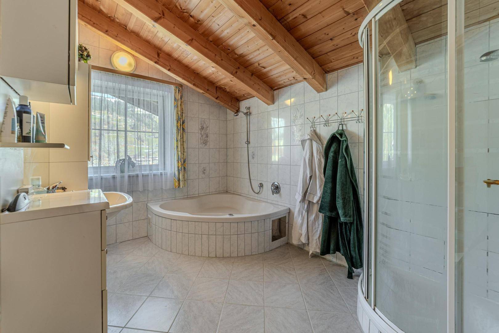 Geräumiges Badezimmer mit Eckbadewanne, Dusche und Fliesenboden unter Holzbalkendecke.