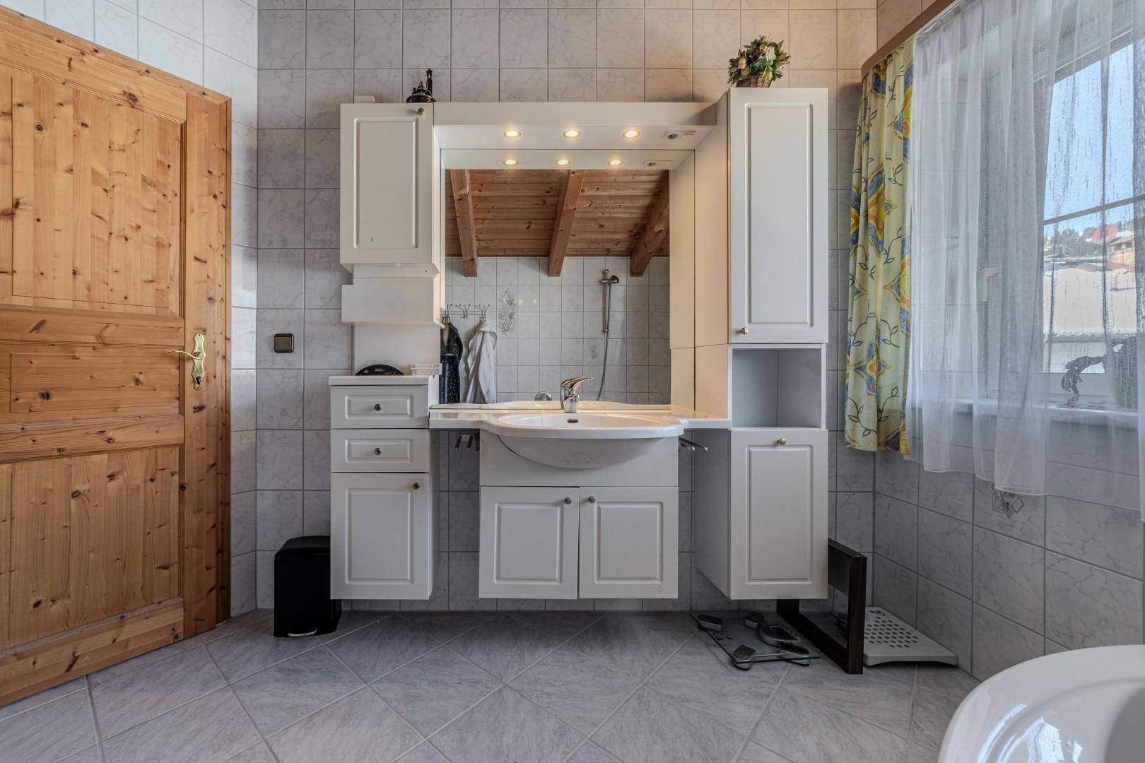 Badezimmer mit modernem Waschtisch, Spiegelschrank und Fenster.