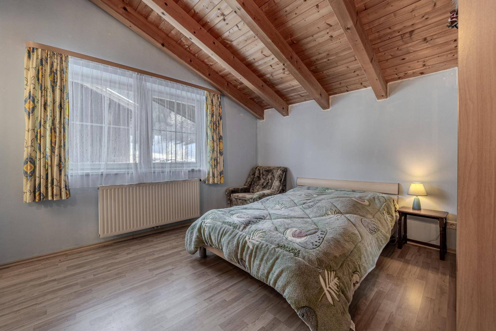 Schlafzimmer im Dachgeschoss mit Holzbalkendecke, Doppelbett und großem Fenster.