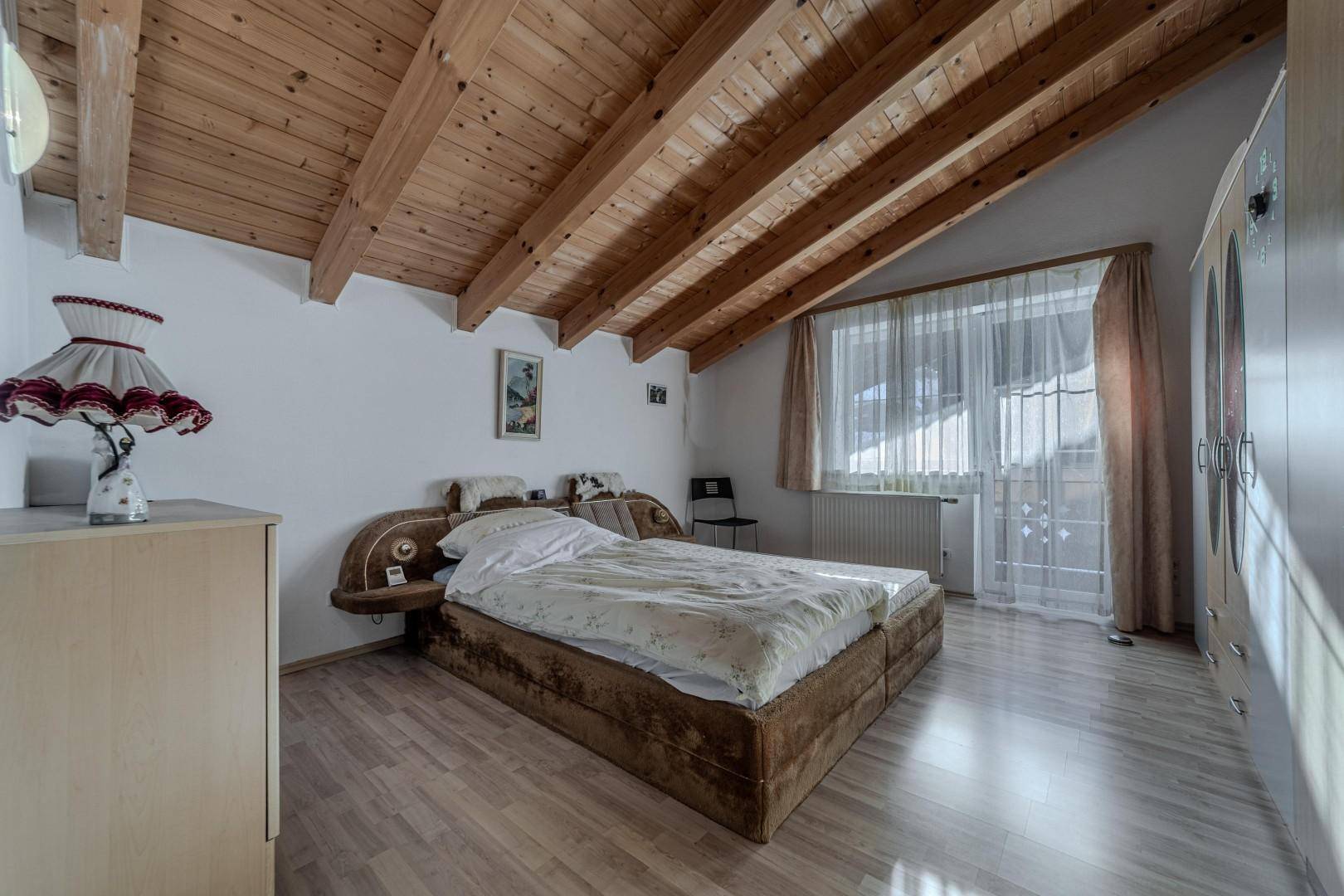 Schlafzimmer mit Holzbalkendecke, Doppelbett und großem Fenster mit Blick nach draußen.