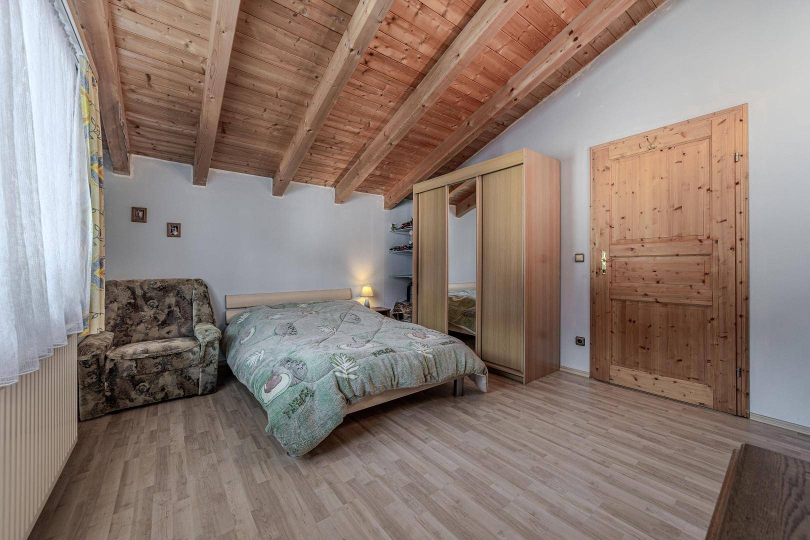 Gemütliches Schlafzimmer mit Holzbalkendecke, Kleiderschrank und Fenster.