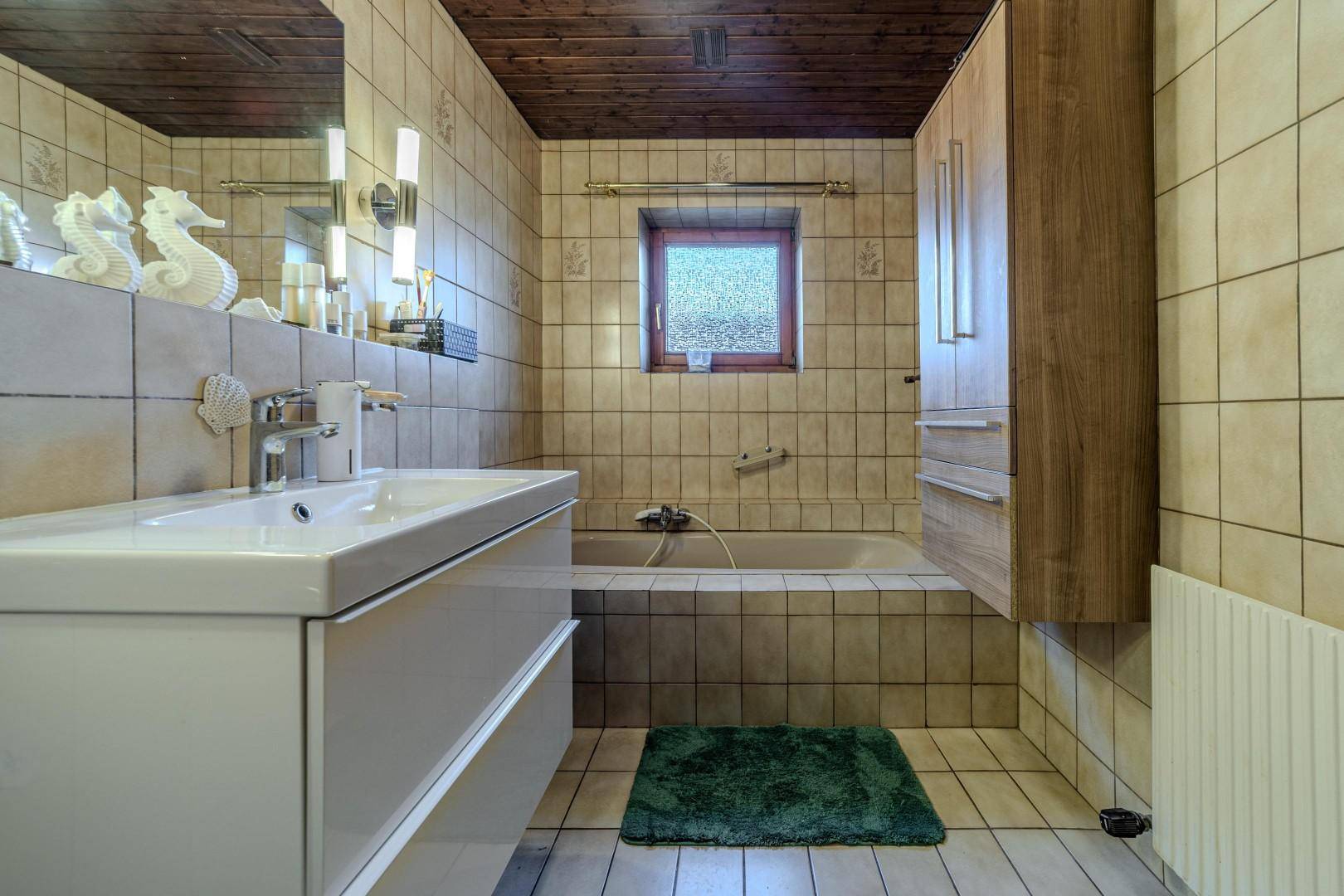 Helles Badezimmer mit beigefarbenen Fliesen, modernem Waschtisch und Badewanne.