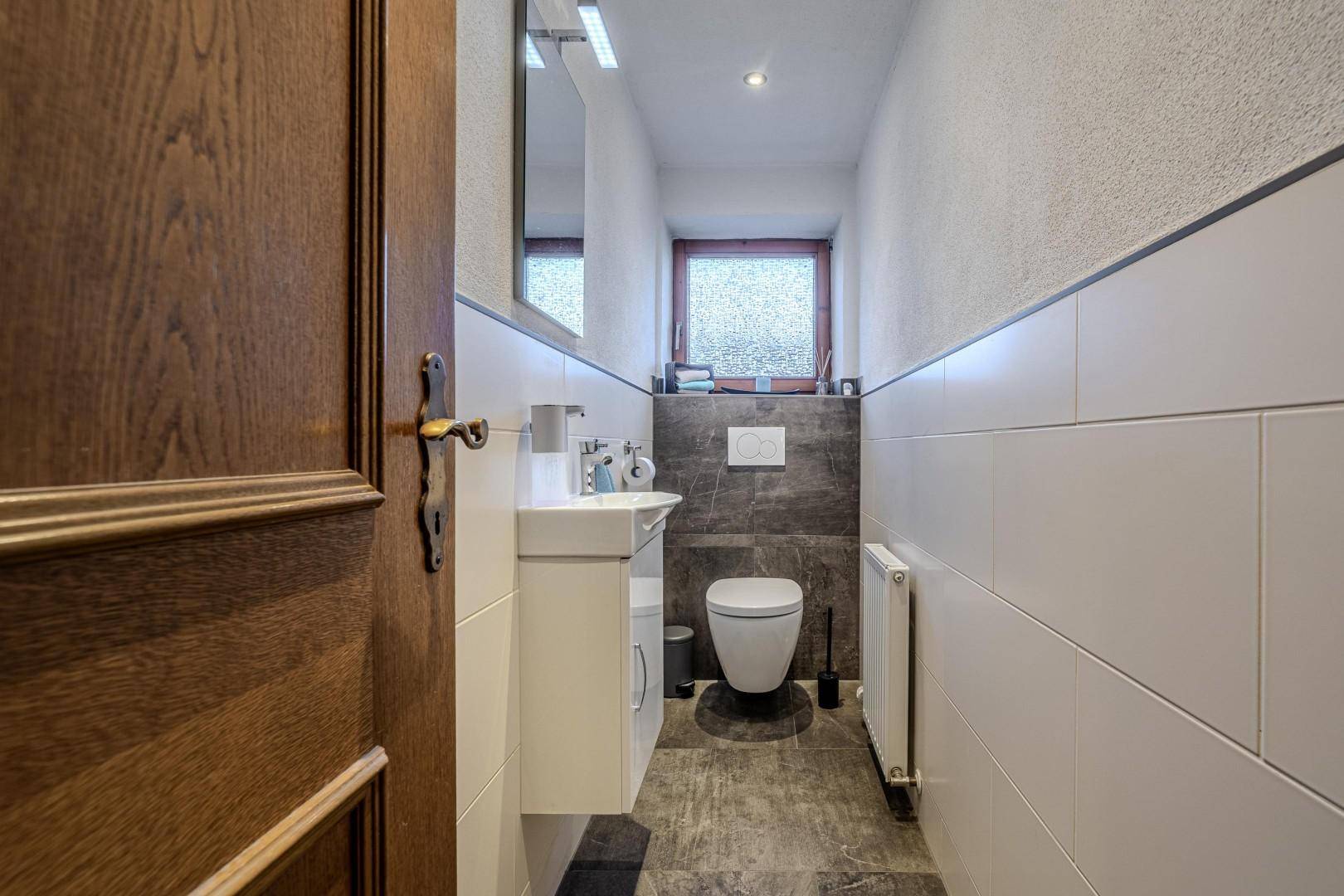 Modernes Gäste-WC mit dunklen Akzentfliesen und wandhängendem WC.