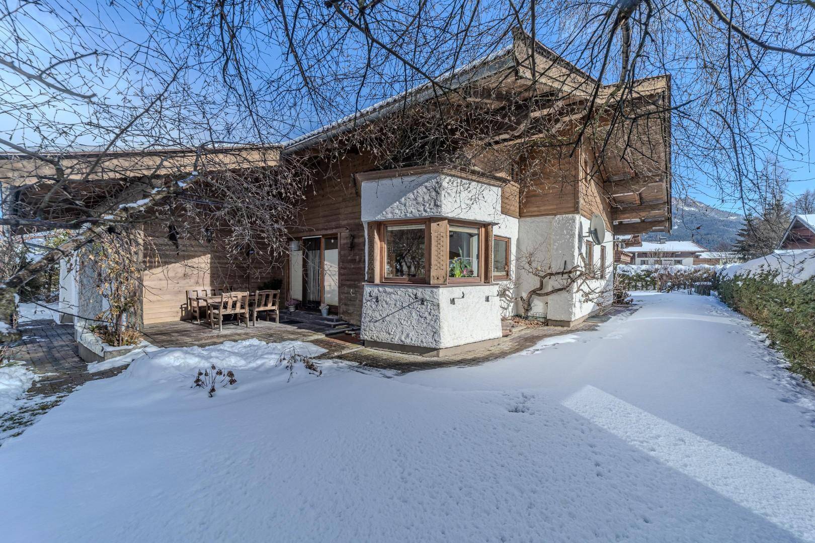 Charmantes Haus im Winter mit Holzfassade, Terrasse und verschneitem Garten.