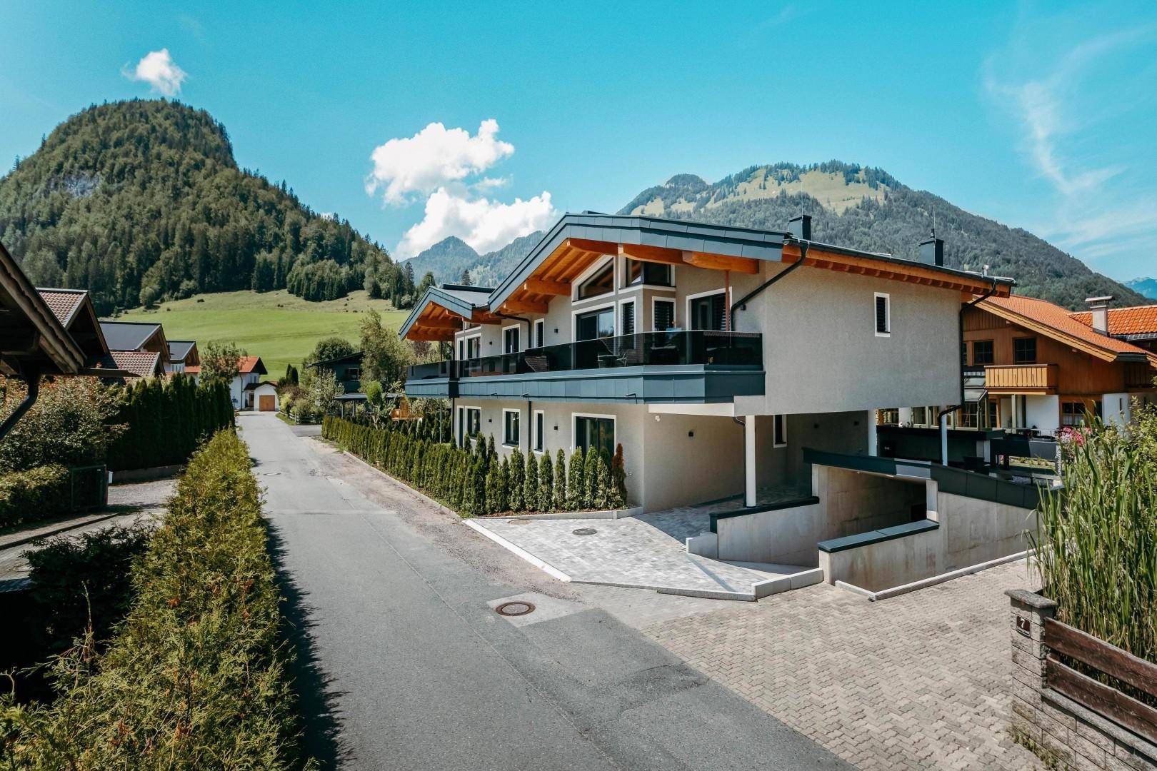 Modernes Wohngebäude mit Balkonen, großen Fenstern und Bergblick in einer alpinen Umgebung.