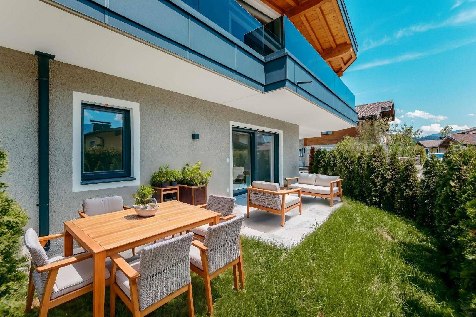 Sonnige Terrasse mit Holztisch, bequemen Gartenmöbeln und gepflegtem Rasen im Grünen.