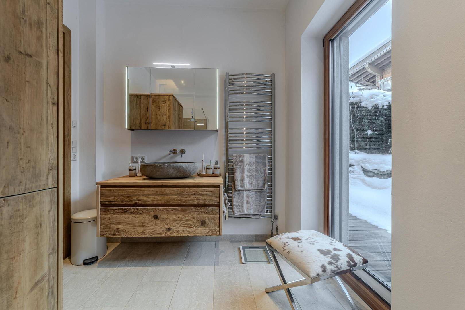 Helles Badezimmer mit Fenster, Holzwaschtisch und Blick auf die verschneite Landschaft.