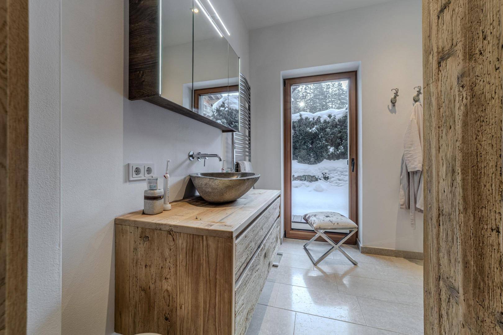 Detailansicht des modernen Badezimmers mit Holzwaschtisch, Aufsatzbecken und Fenster.